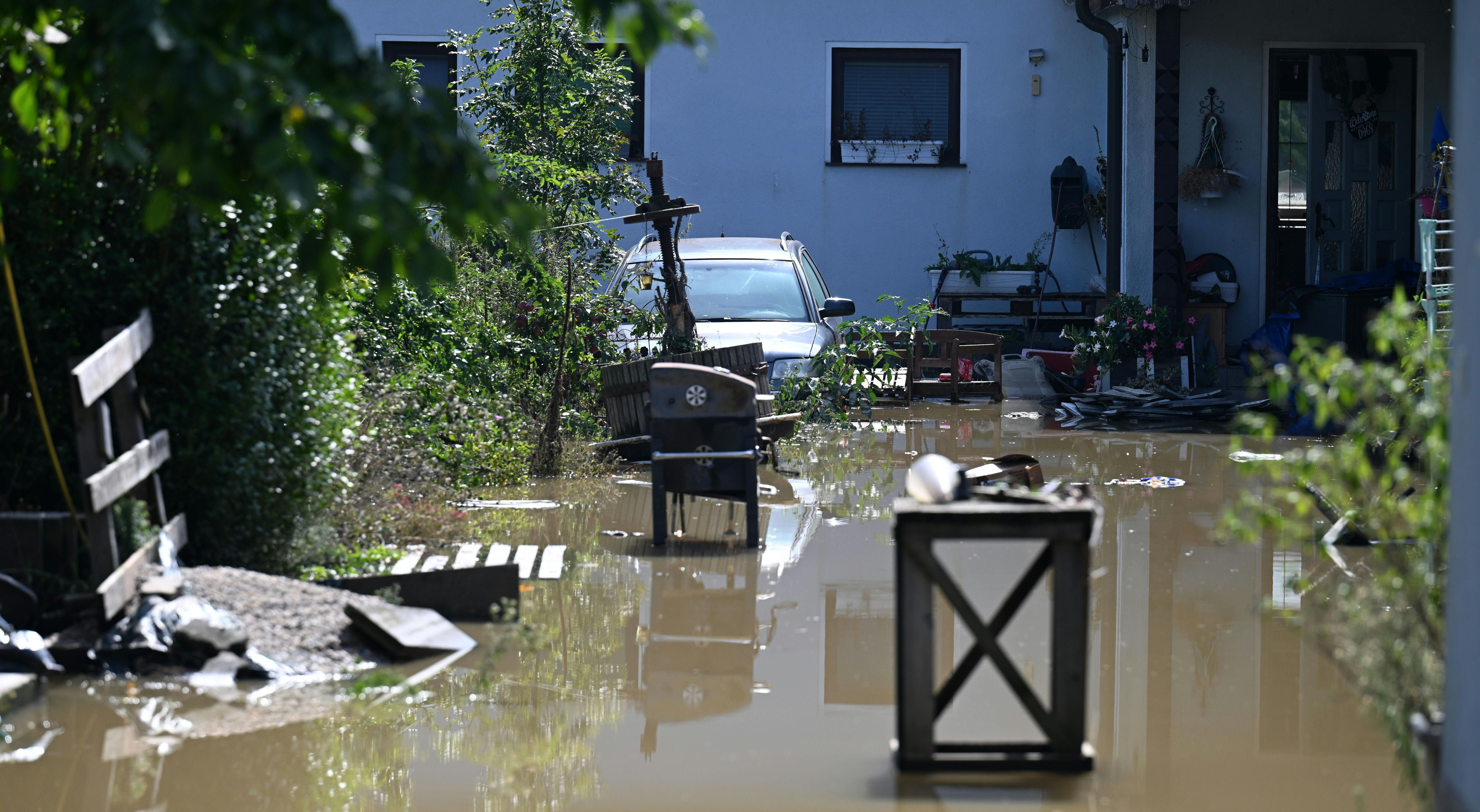 Überfluteter Hof mit Auto, Möbeln und Pflanzen nach Hochwasser in Moosbierbaum, Niederösterreich.