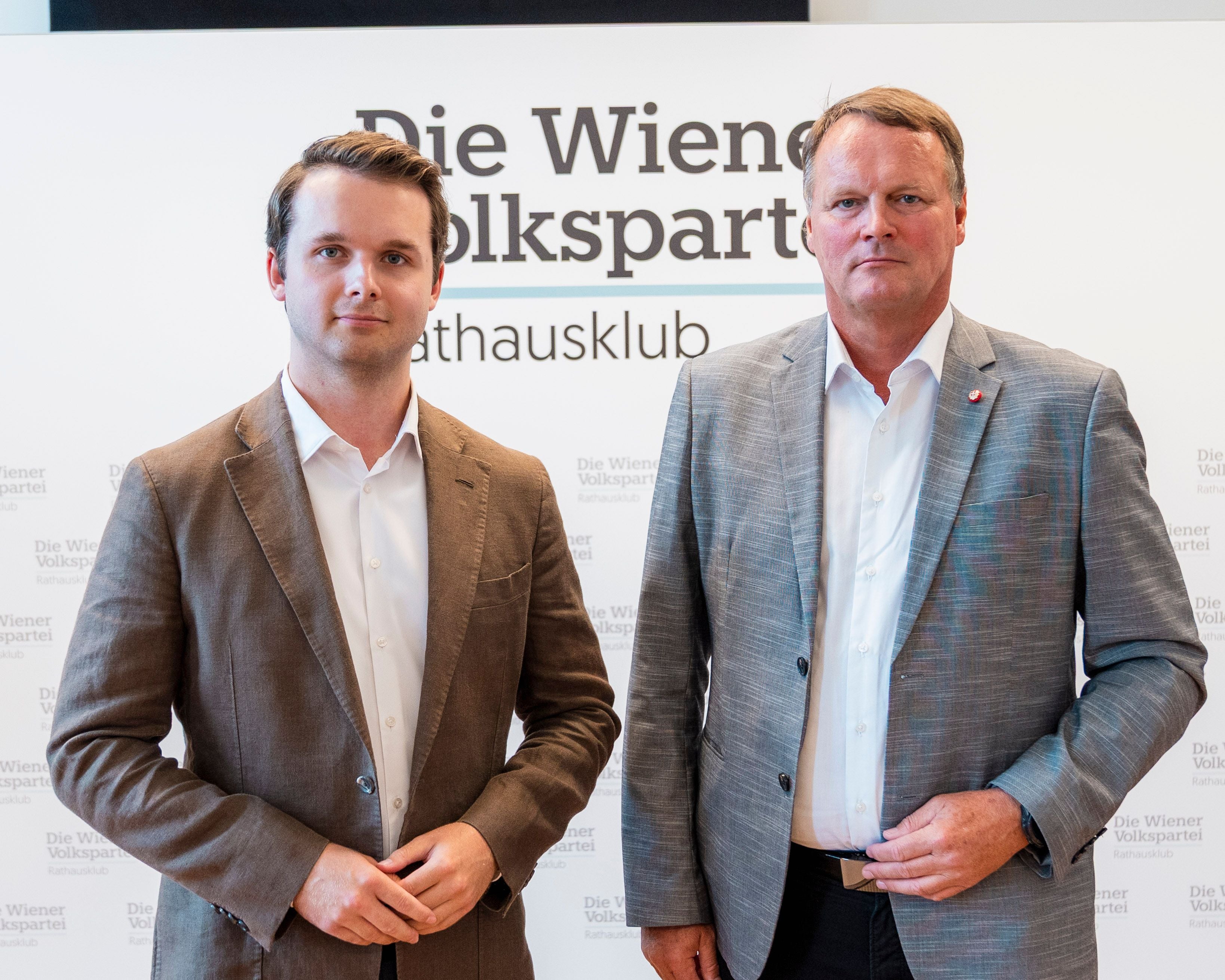 Zwei Männer im Anzug stehen vor einem Schild der Wiener Volkspartei.