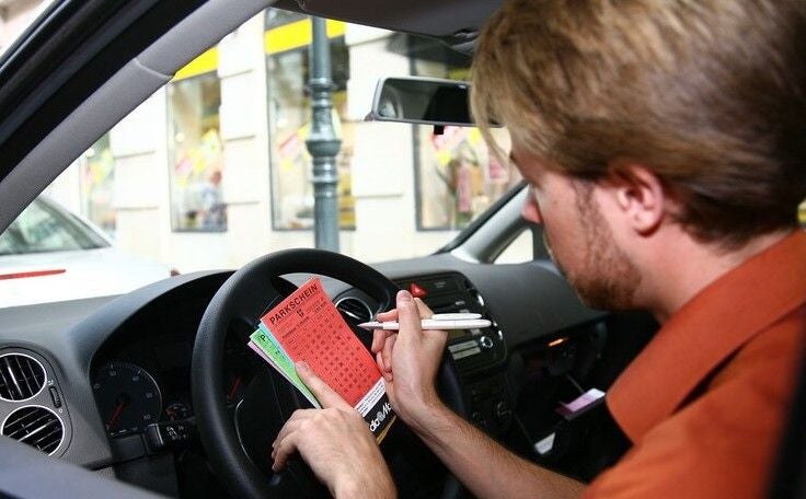 Ein Mann füllt in einem Auto einen Wiener Parkschein auf dem Lenkrad aus.