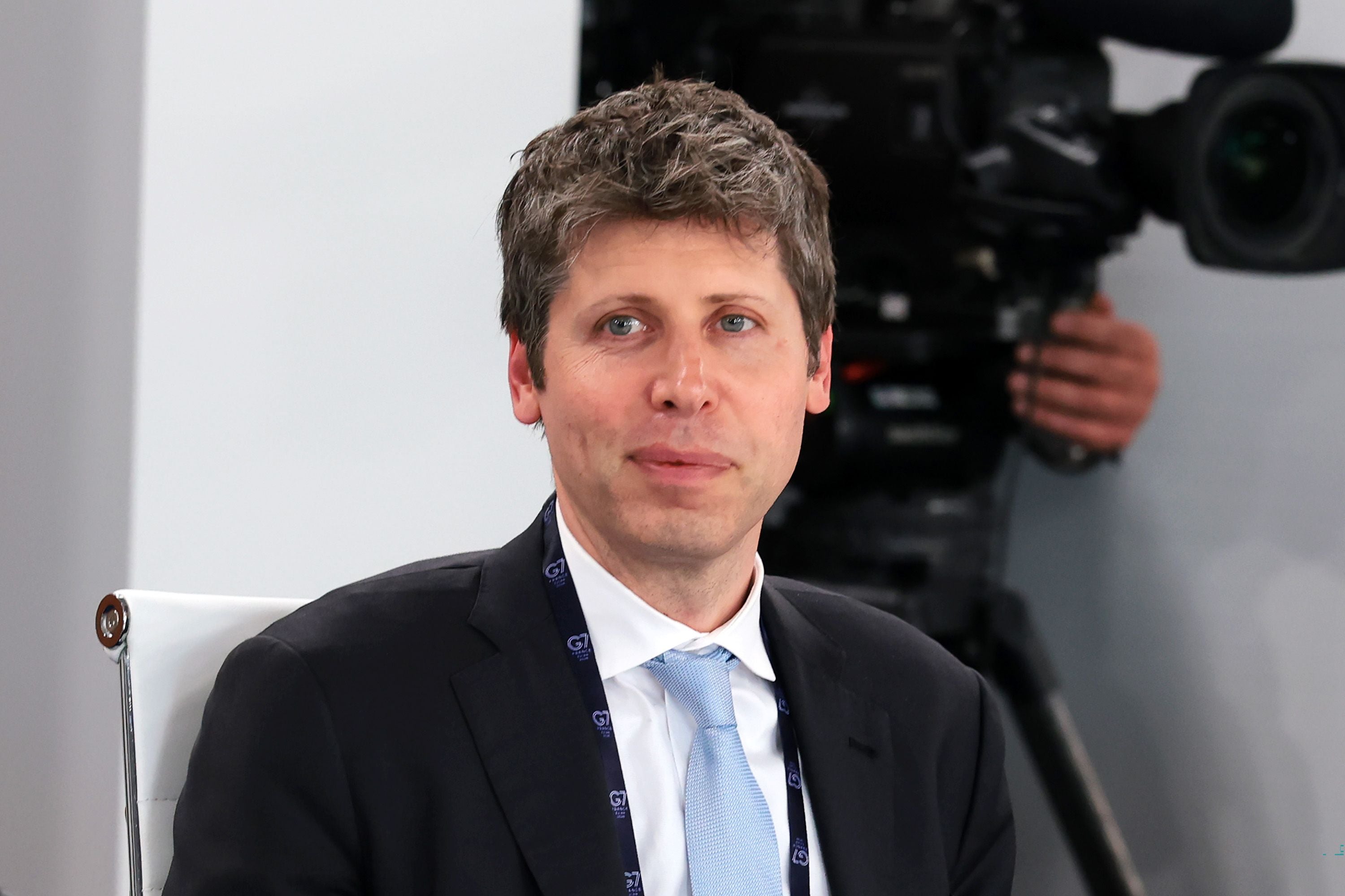 Ein Mann im Anzug sitzt auf einem weißen Stuhl, im Hintergrund eine große TV-Kamera.