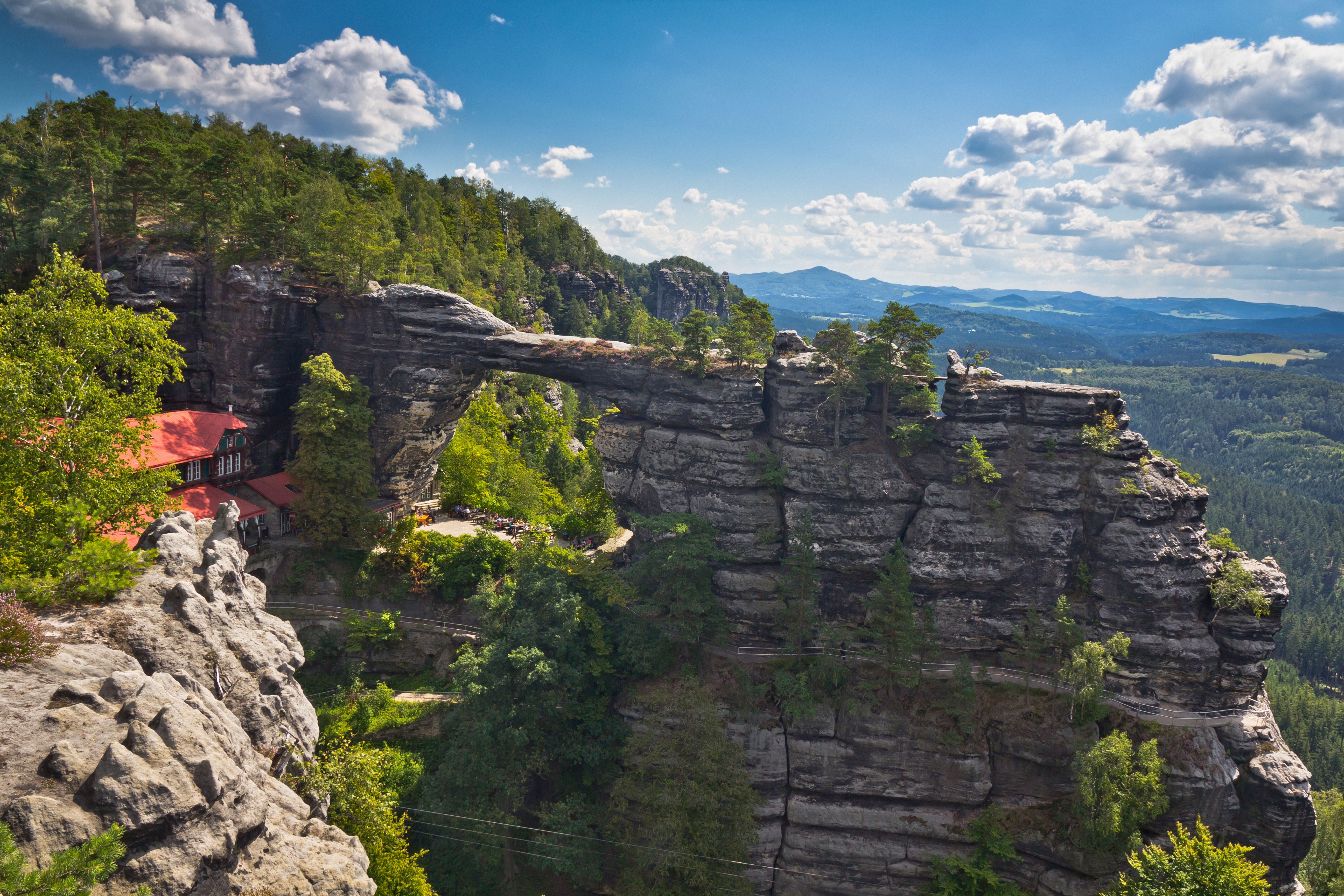Die Pravcická brána, eine große Sandstein-Felsbrücke inmitten grüner bewaldeter Berge.