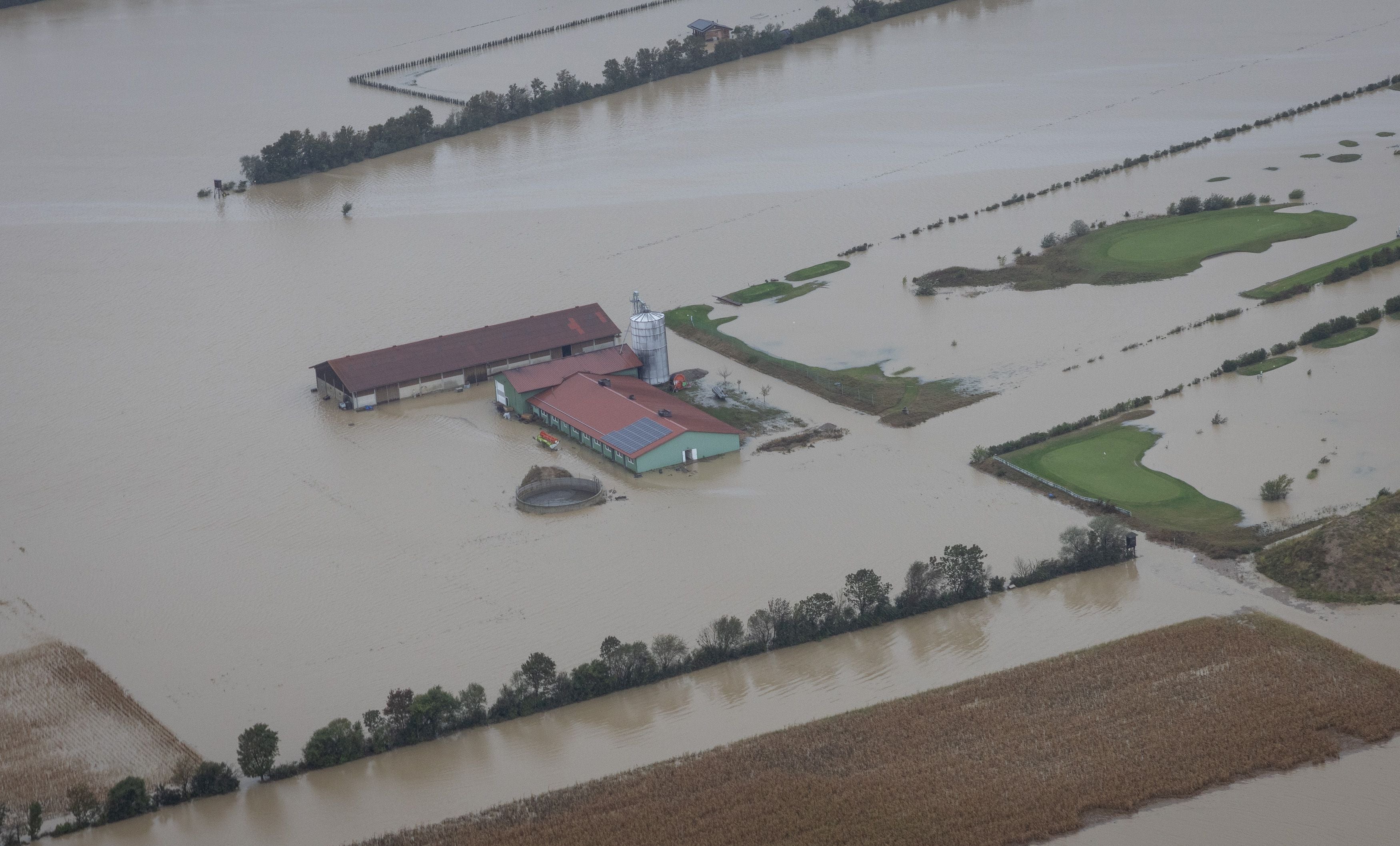 Überflutetes landwirtschaftliches Gebäude und umliegende Felder nach starkem Regen.