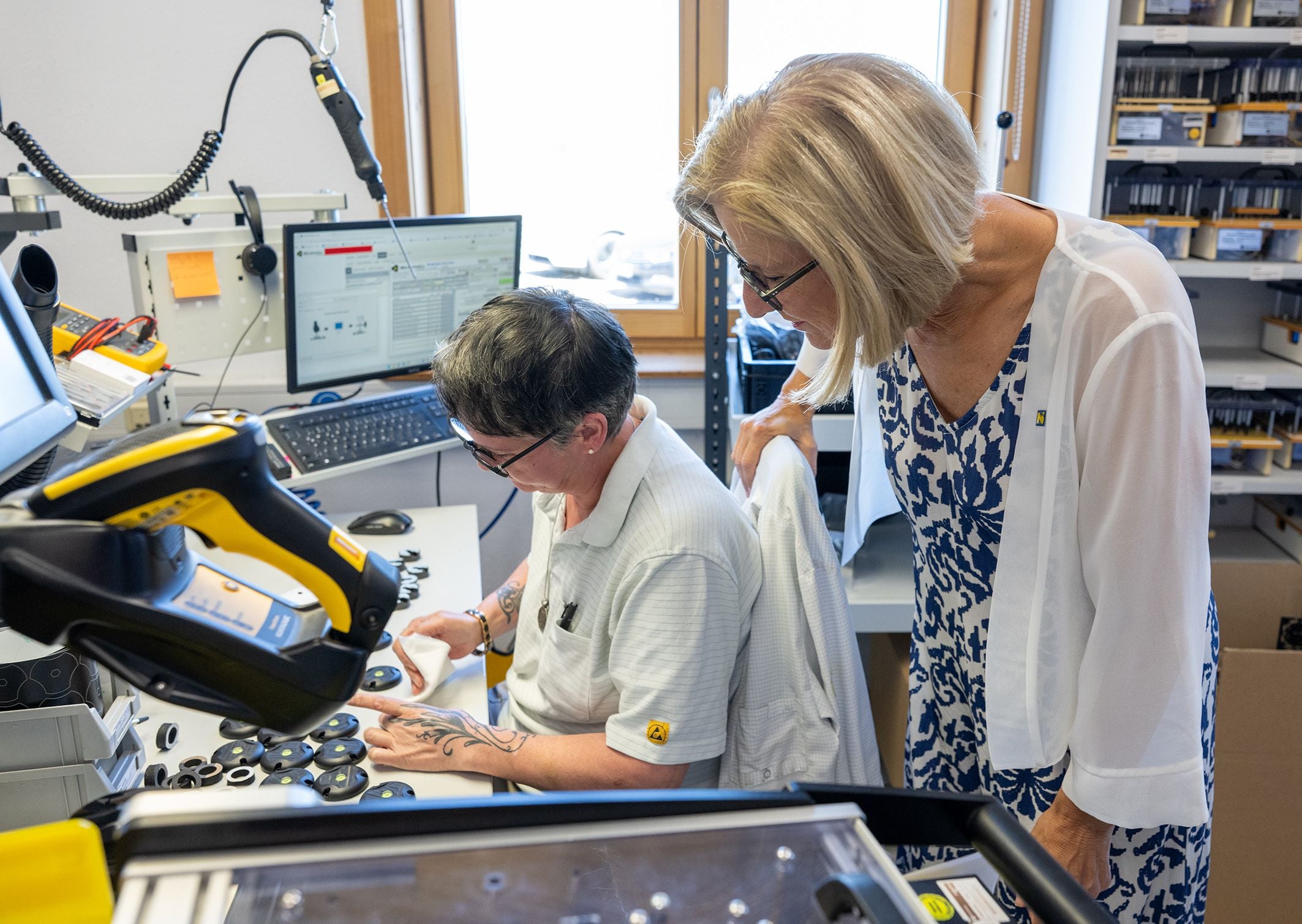 Zwei Frauen arbeiten an einem Schreibtisch mit technischen Geräten und Computern in einem Büro.