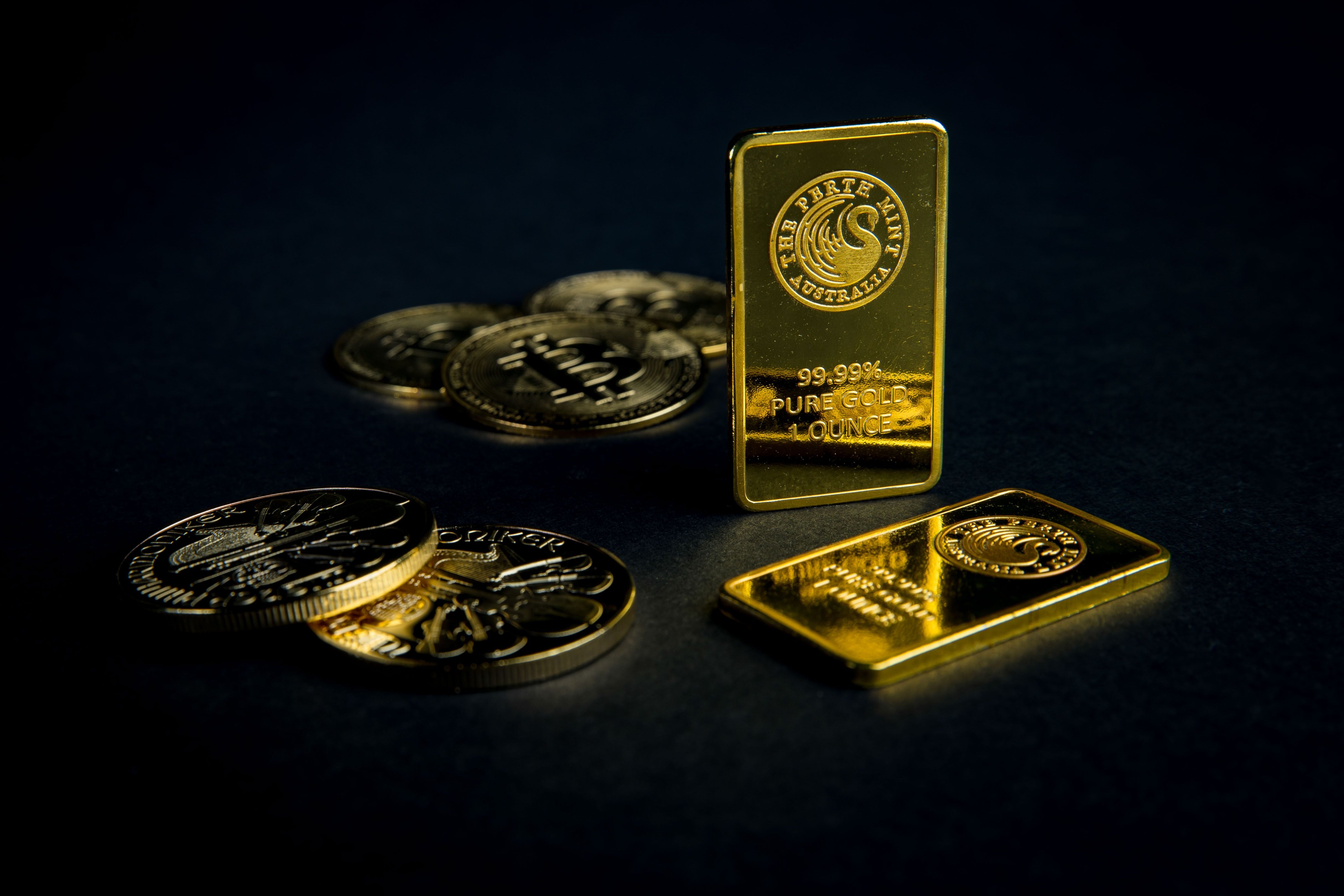 Goldbarren und mehrere Goldmünzen liegen auf dunklem Hintergrund.