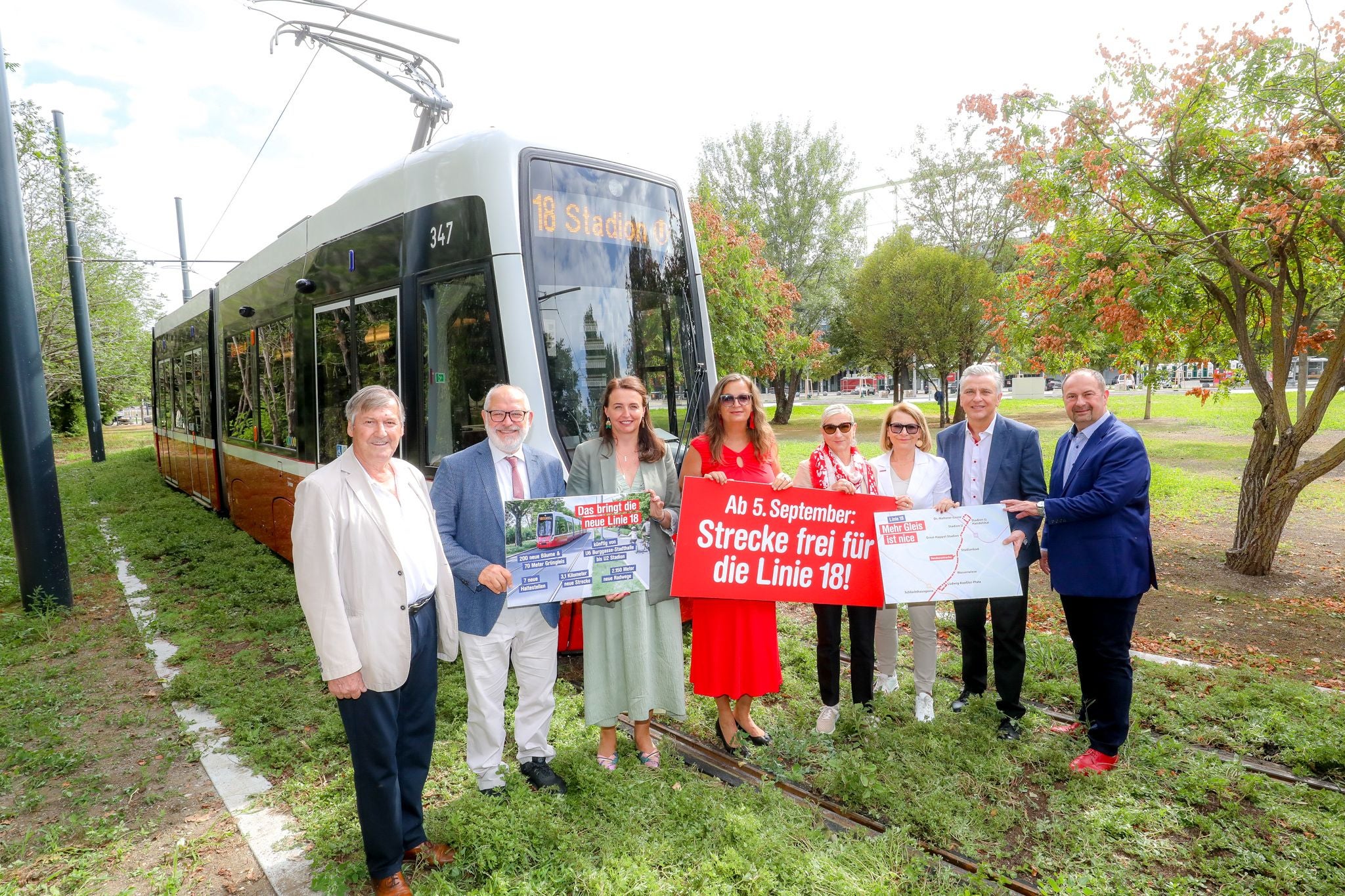 Mehrere Menschen stehen vor einer Straßenbahn der Linie 18 und halten Infoplakate hoch.