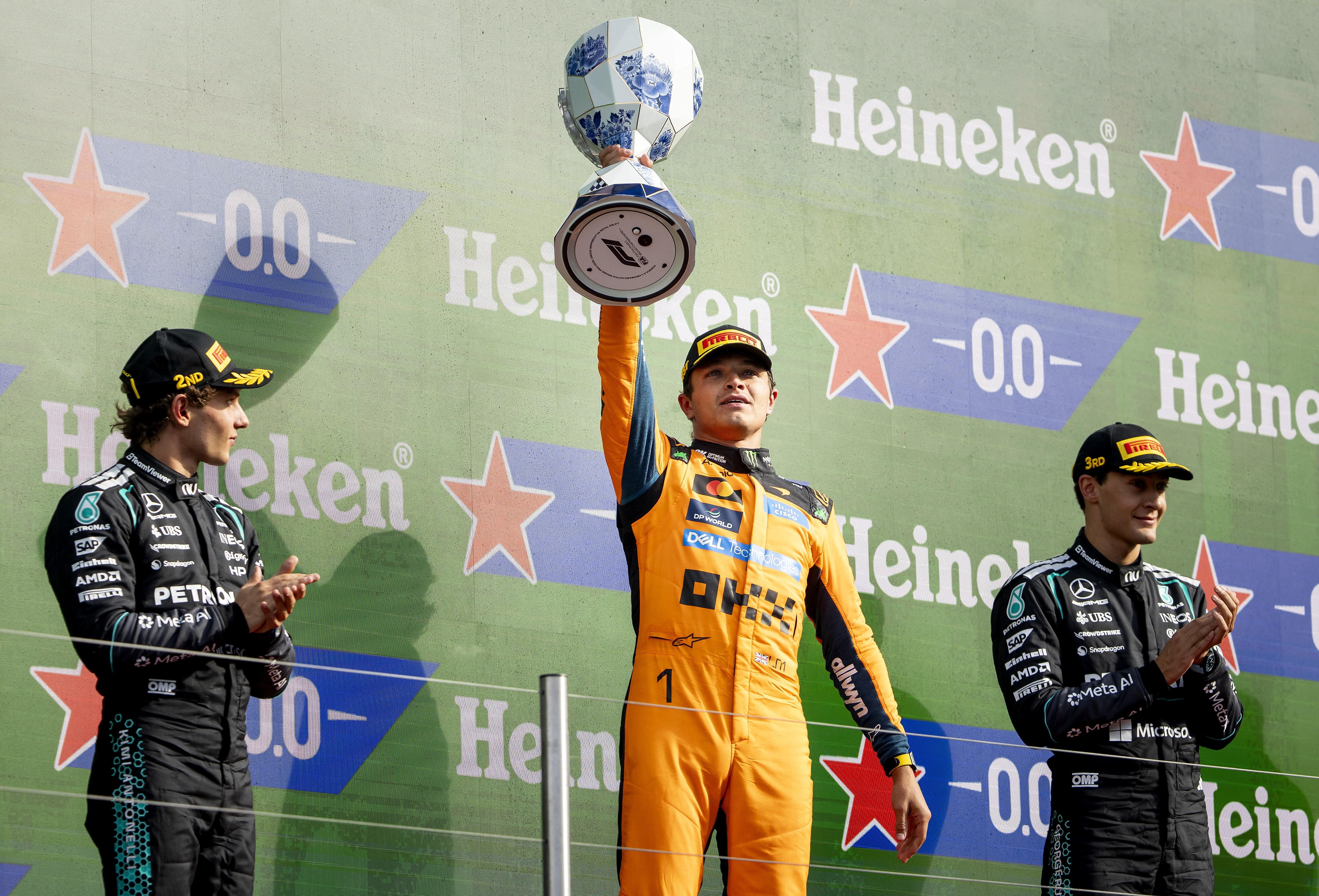 Drei Formel-1-Fahrer feiern auf dem Siegerpodest, einer hält einen Pokal hoch.