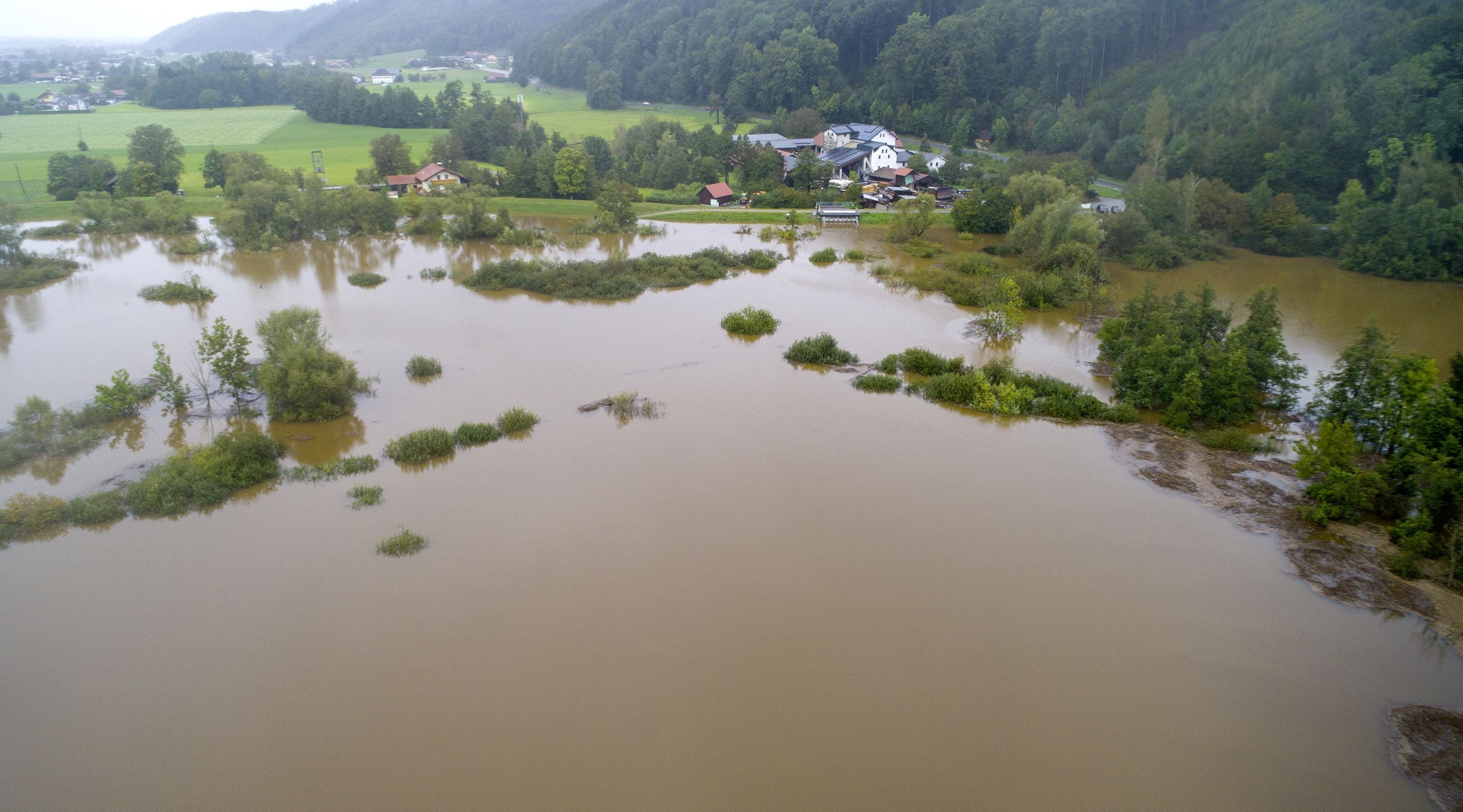 Überflutete Landschaft in Lengau mit teilweise unter Wasser stehenden Bäumen und Häusern im Hintergrund.