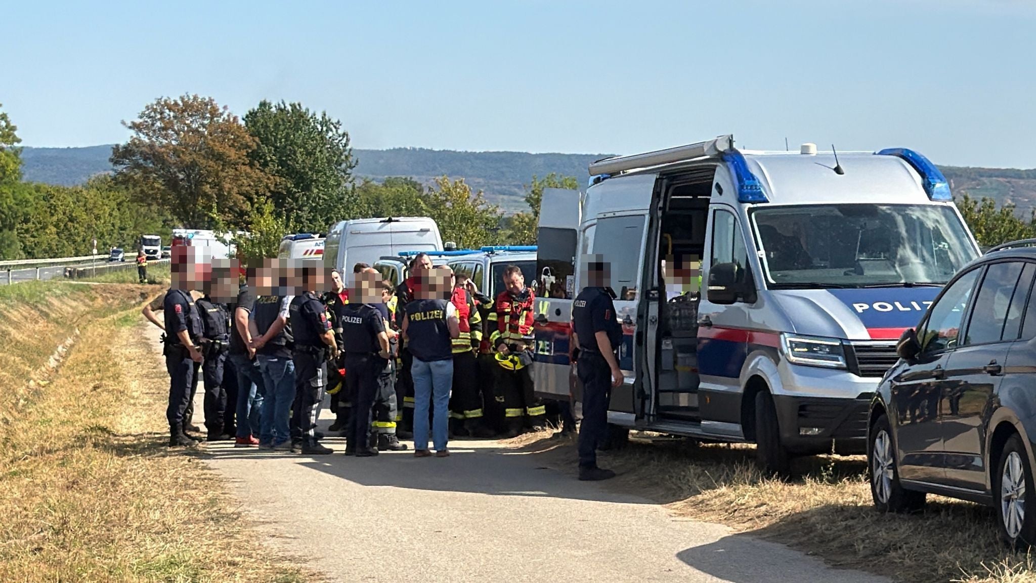 Mehrere Polizisten und Feuerwehrleute stehen bei Einsatzfahrzeugen am Straßenrand.