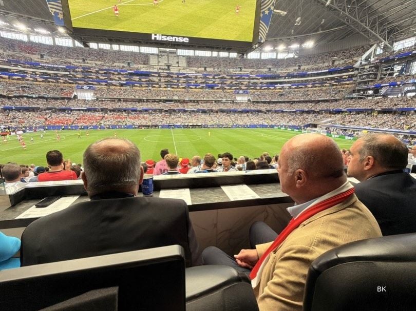 Zuschauer sitzen in einer VIP-Loge in einem vollen Stadion bei einem WM-Fußballspiel.
