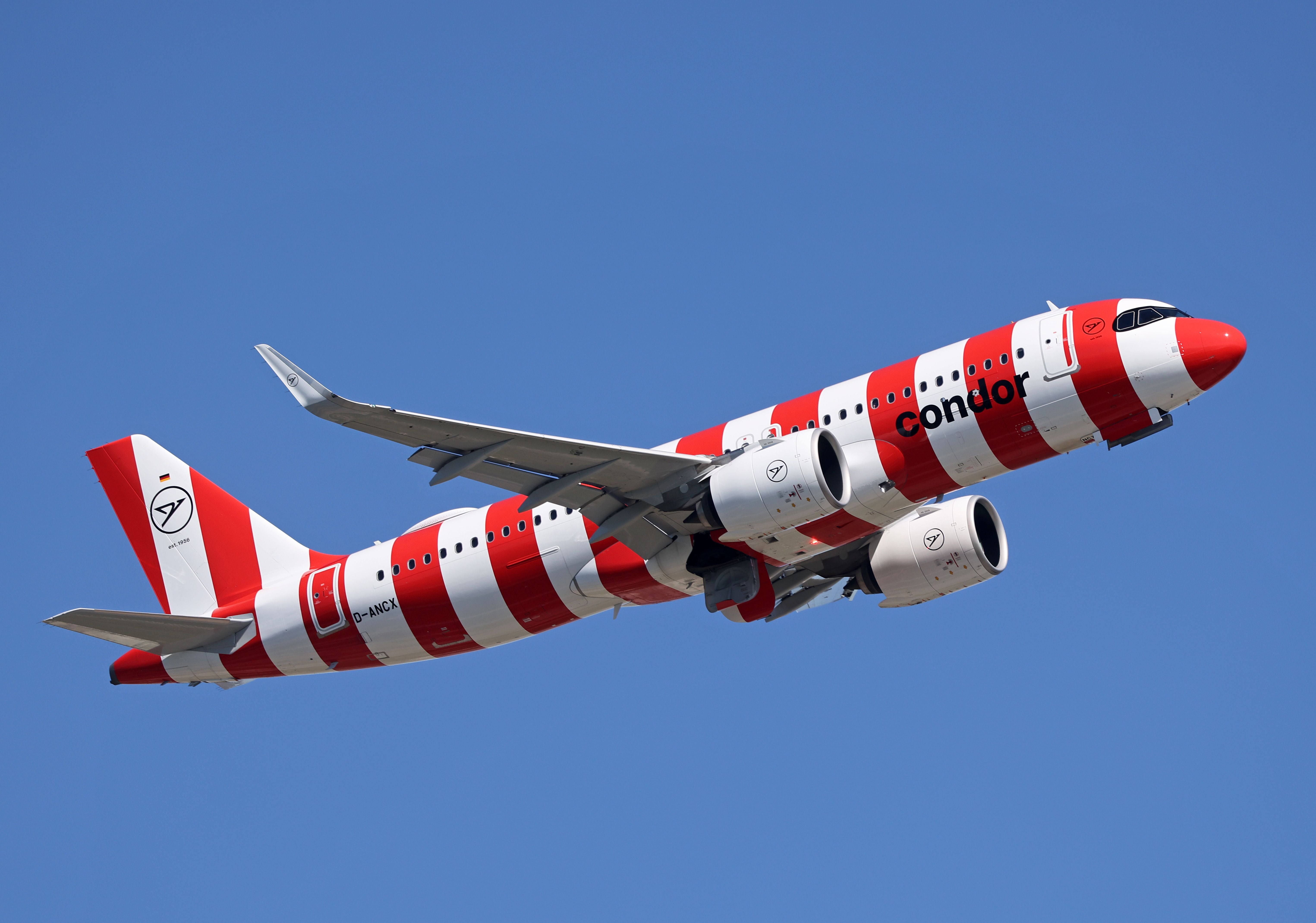 Ein Condor Airbus A320 im rot-weiß gestreiften Design startet vor blauem Himmel.