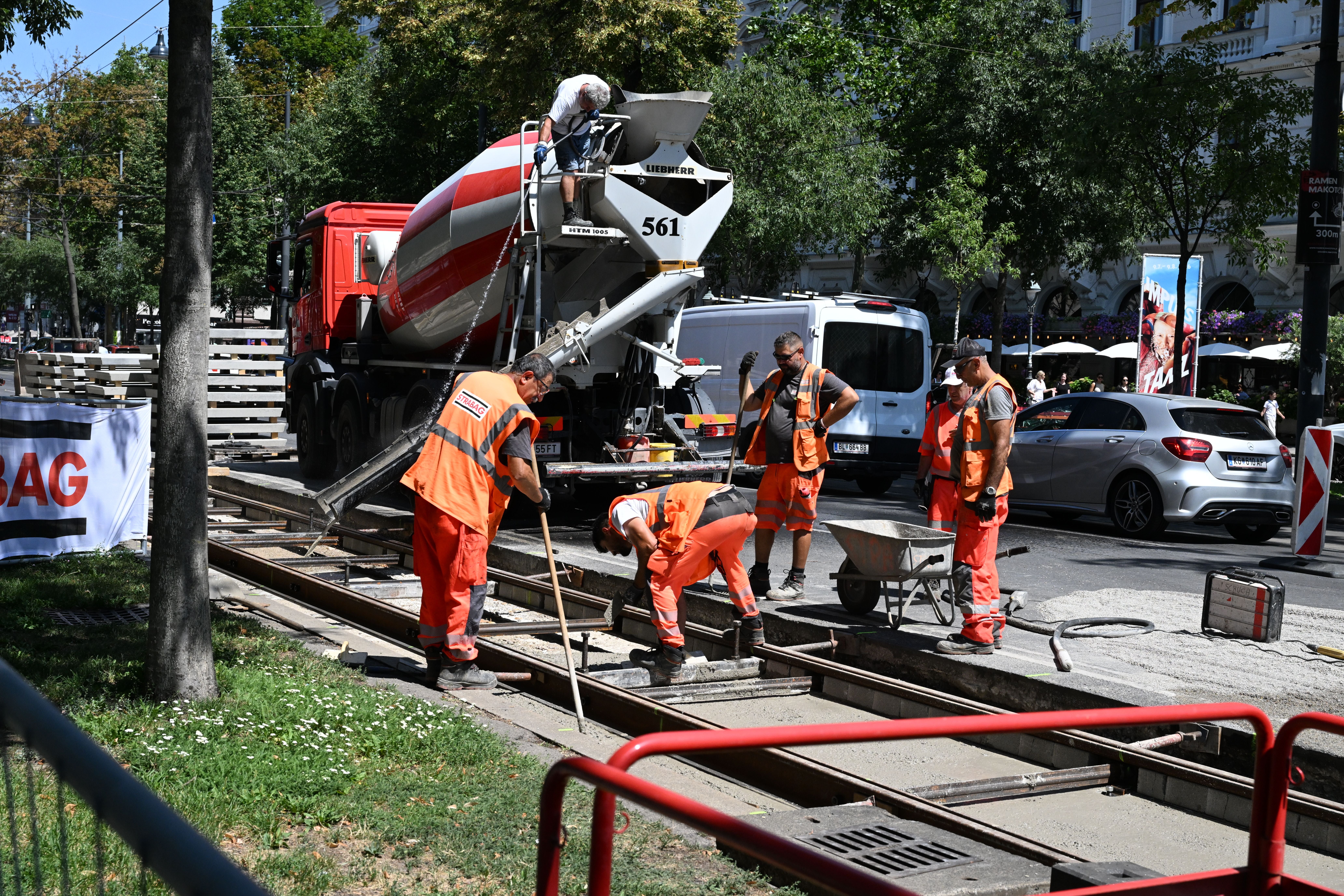 Bauarbeiter gießen und verteilen Beton an einer Straßenbahnschiene bei einer Baustelle.