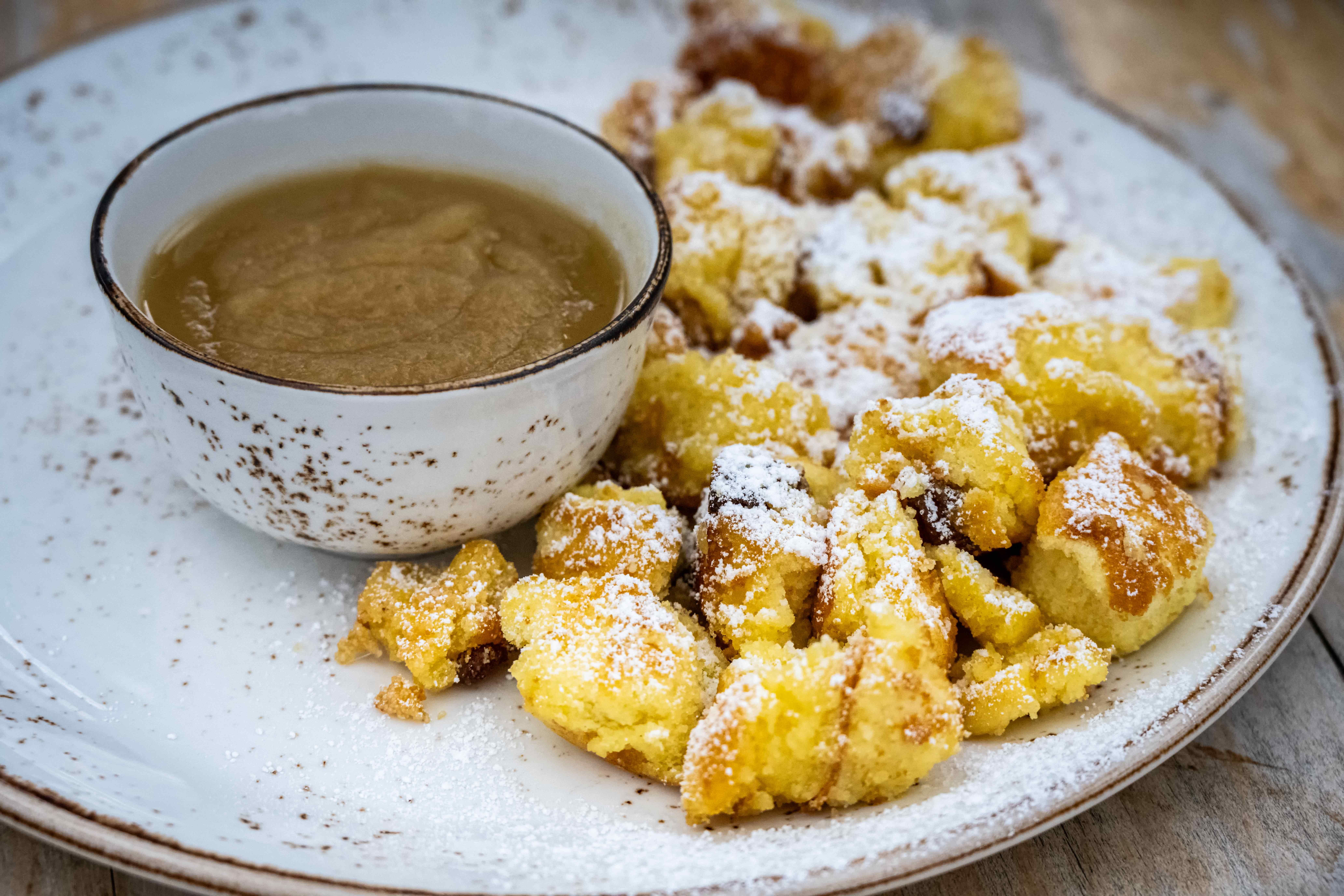 Kaiserschmarrn mit Puderzucker und einer Schale Apfelmus auf einem weißen Teller.