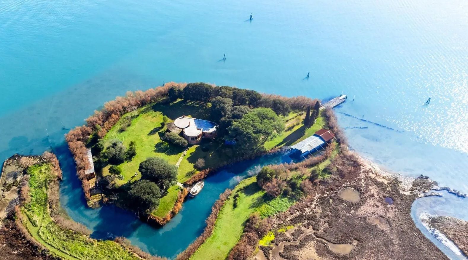 Luftaufnahme der Isola di Crevan mit Haus, viel Grün und Bootssteg im blauen Wasser.