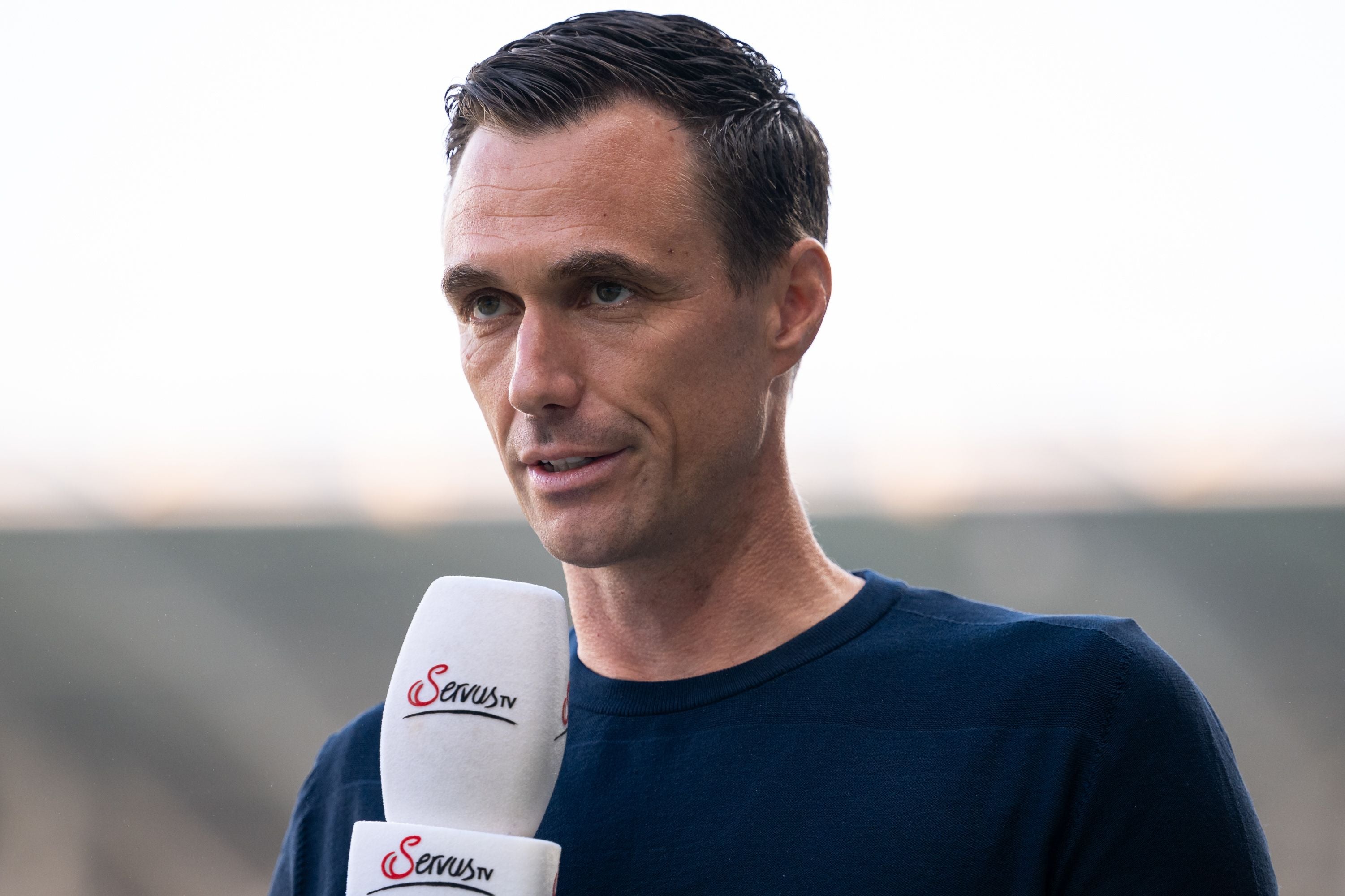Ein Mann hält ein ServusTV-Mikrofon und gibt ein Interview im Freien.
