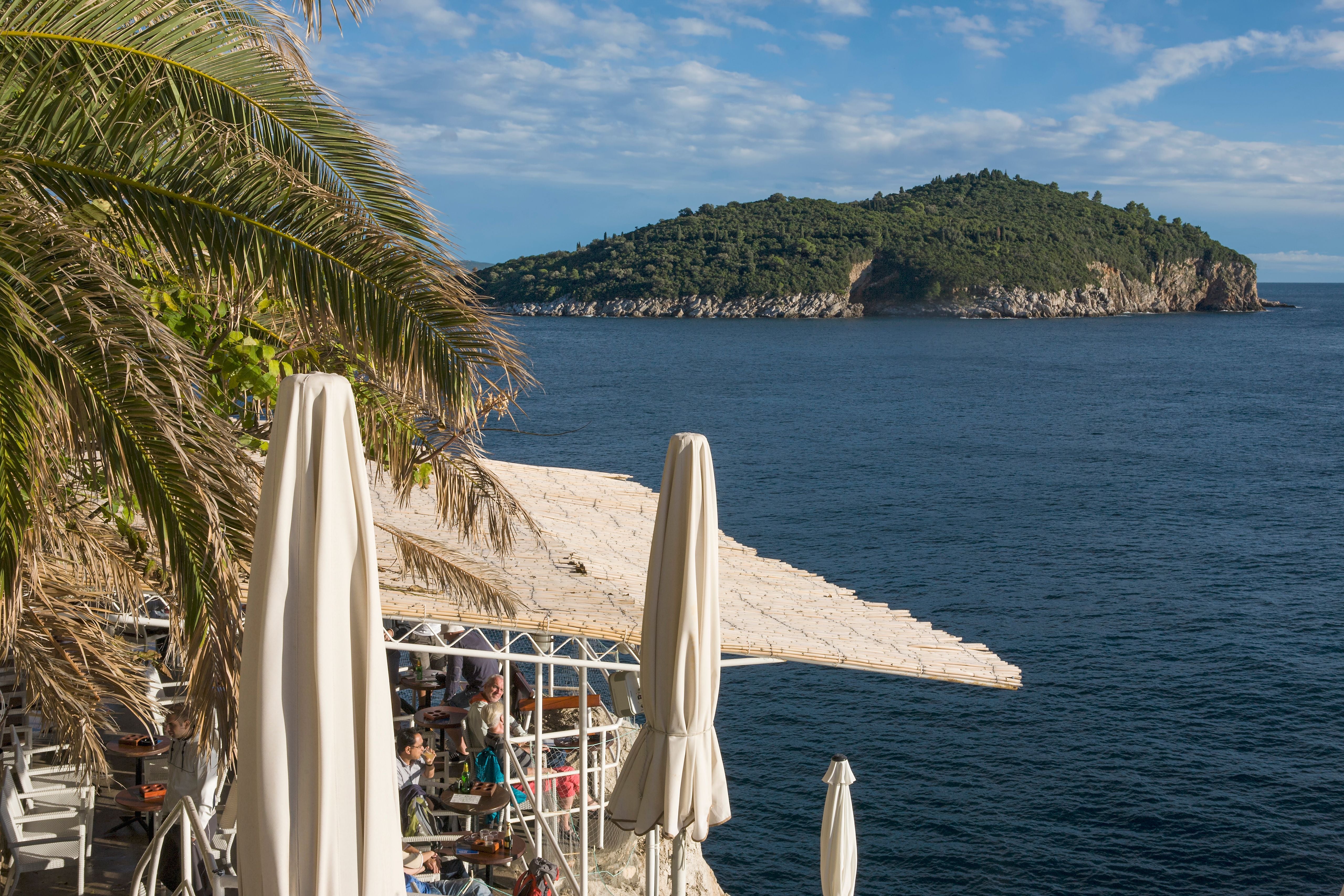 Küstenbar unter Palmen mit Blick auf die Adria und die grüne Insel Lokrum bei Dubrovnik.