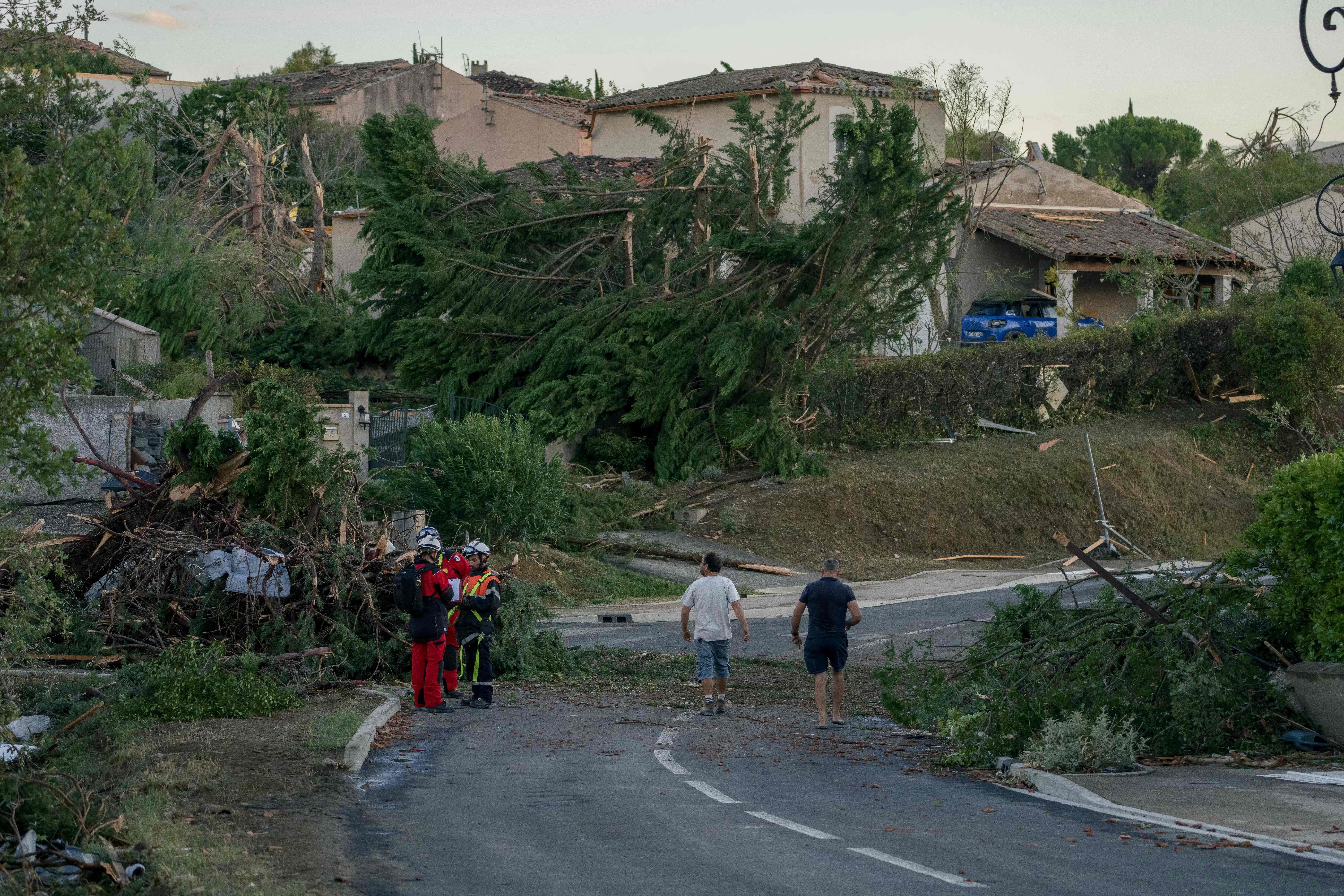 Zerstörte Häuser und umgestürzte Bäume nach einem Tornado, Helfer und Anwohner auf der Straße.