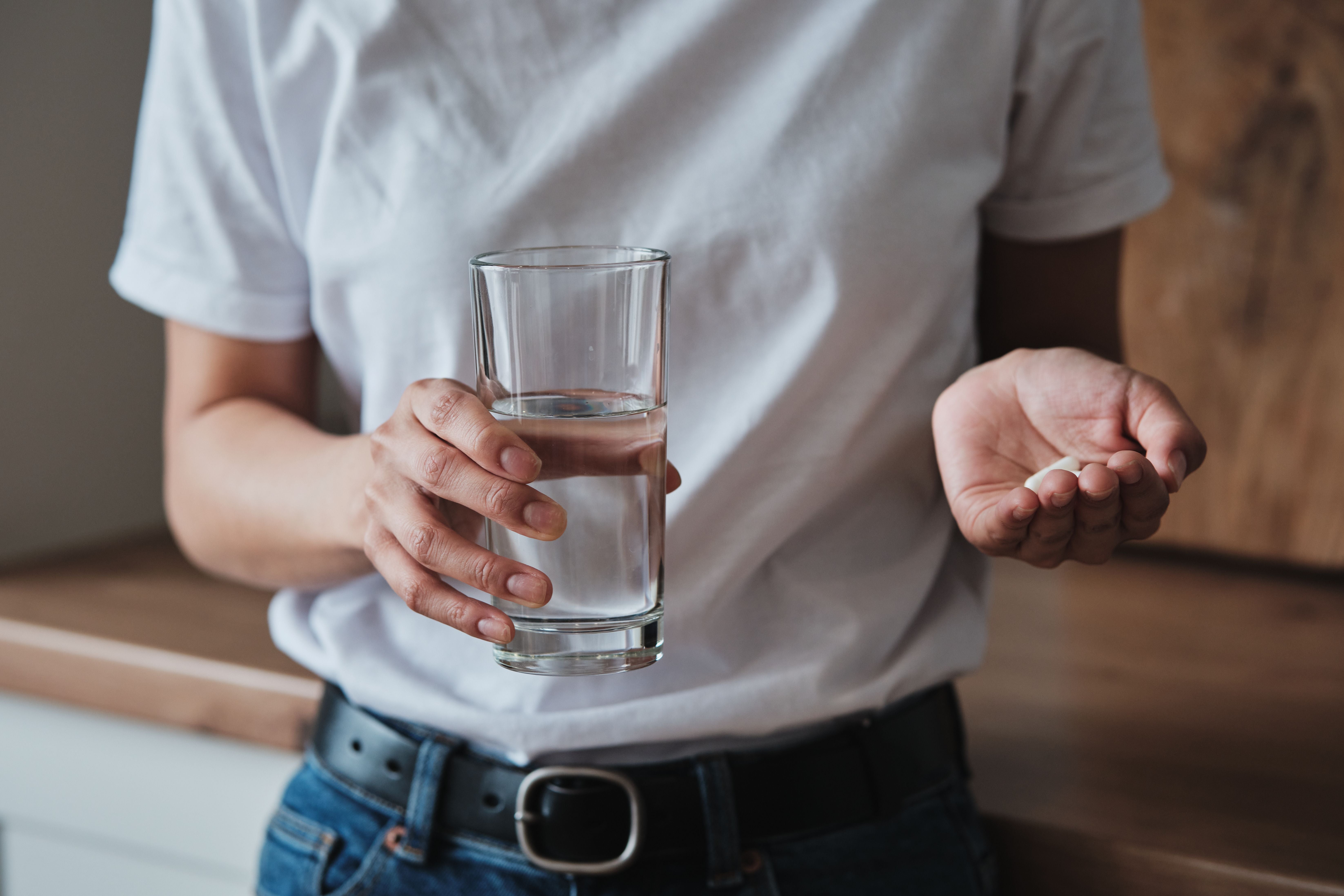 Frau hält mehrere Tabletten in der einen Hand und ein Glas Wasser in der anderen.
