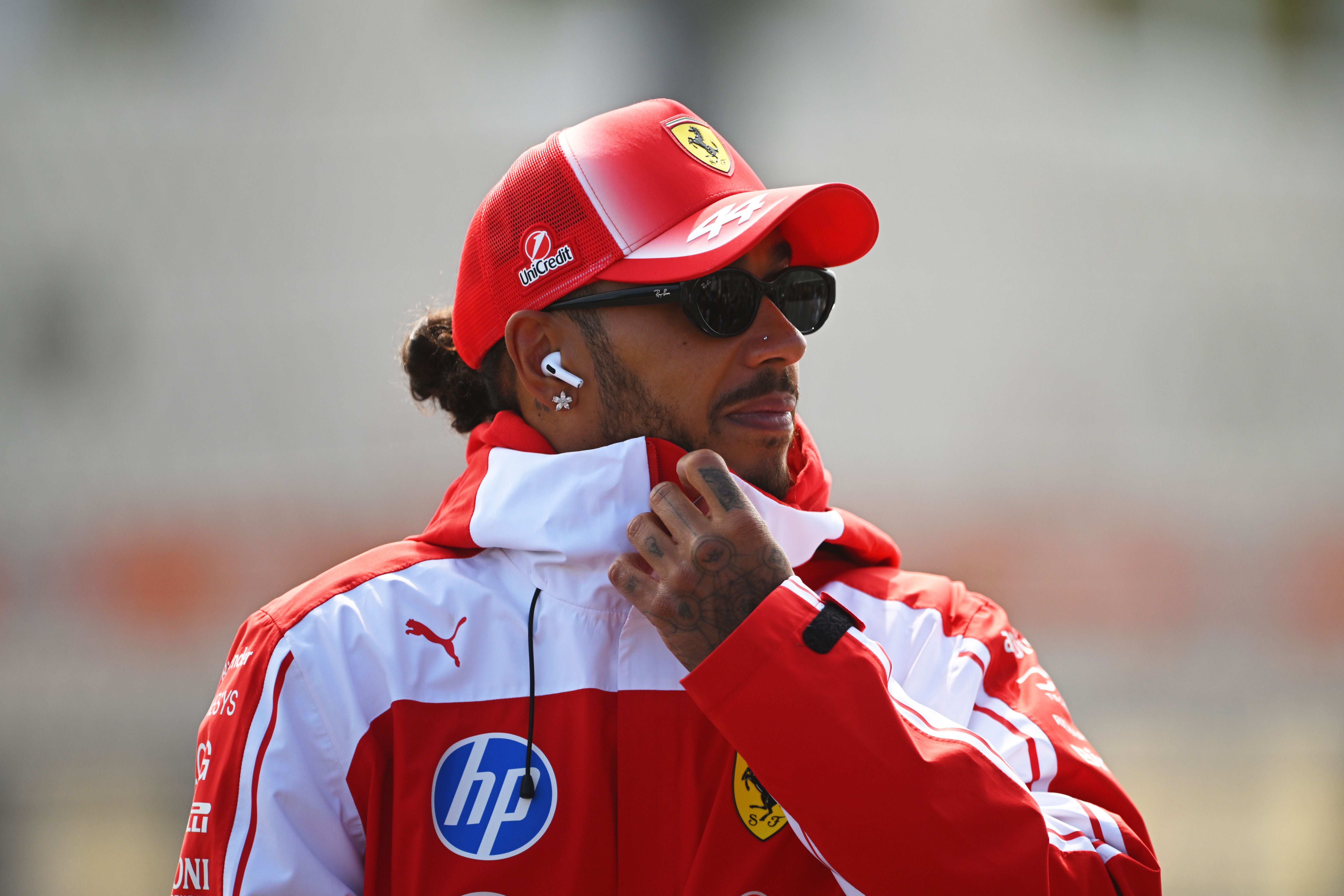 Eine Person in Ferrari-Teamkleidung trägt Sonnenbrille und Mütze bei einer Veranstaltung.