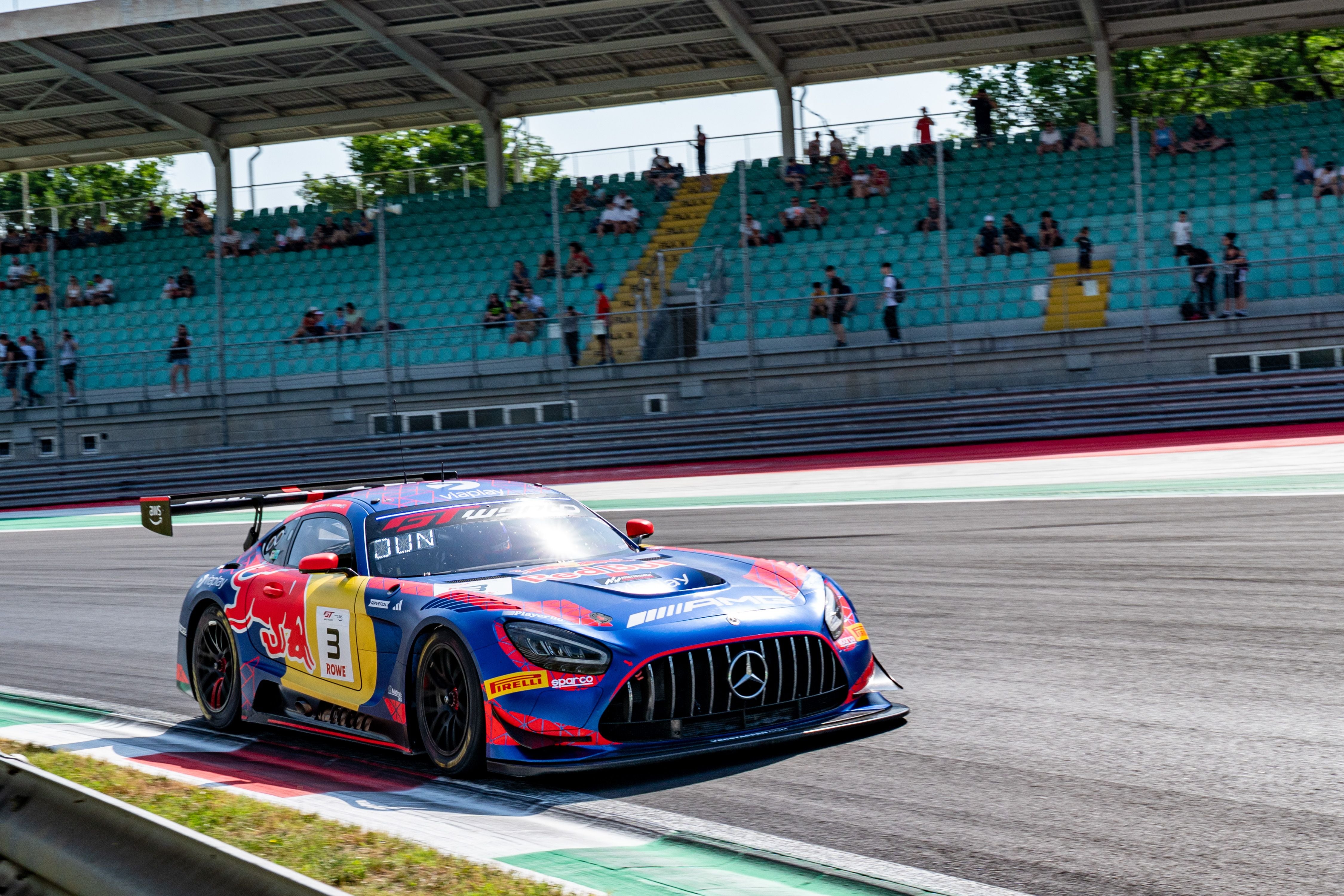 Ein Mercedes-AMG GT3 Rennwagen fährt auf der Rennstrecke in Monza, die Tribünen sind teils besetzt.