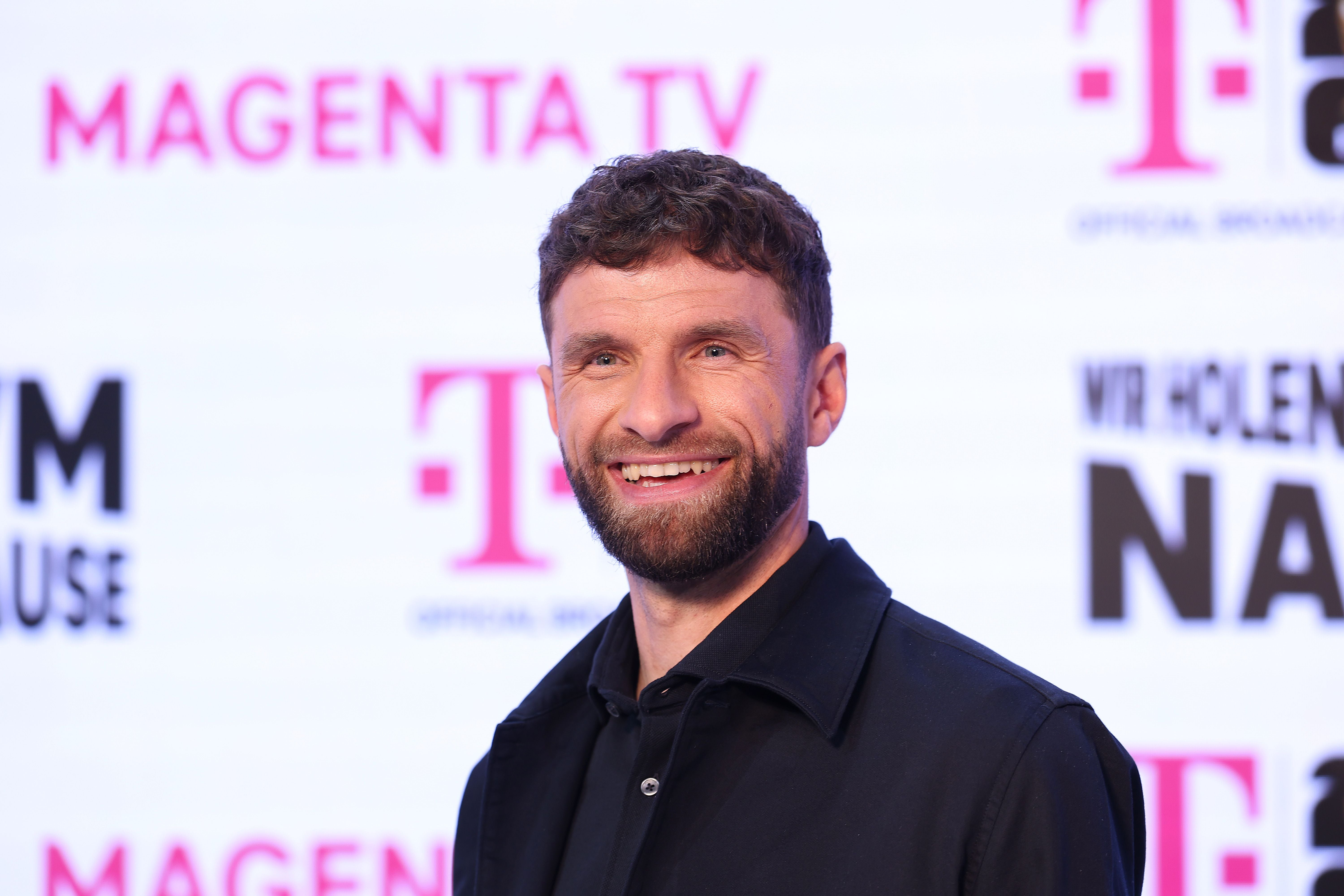 Ein Mann mit Bart lächelt auf einem Event vor einem Hintergrund mit MagentaTV-Logos.
