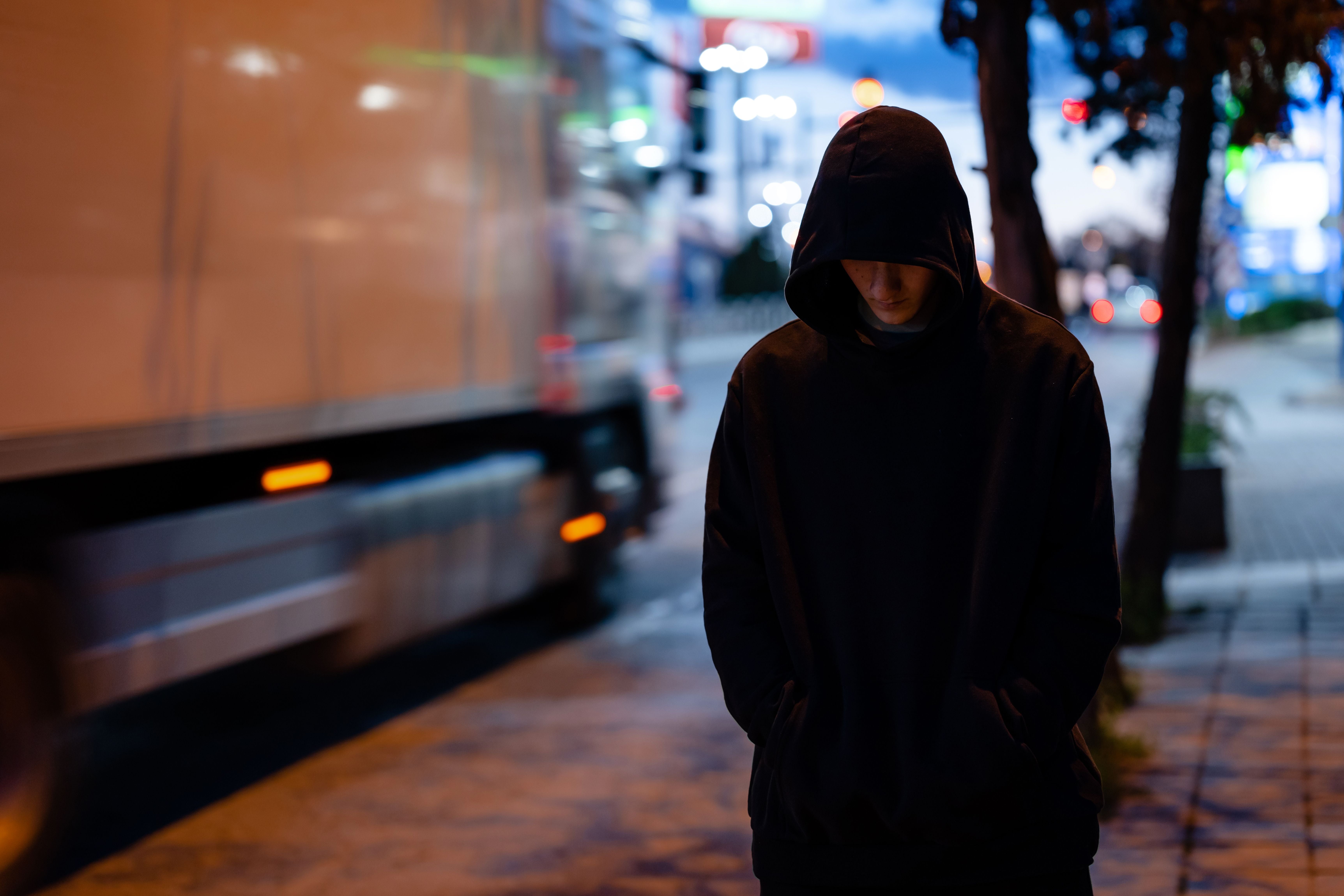 Person mit schwarzem Hoodie steht nachts auf einer beleuchteten Stadtstraße.