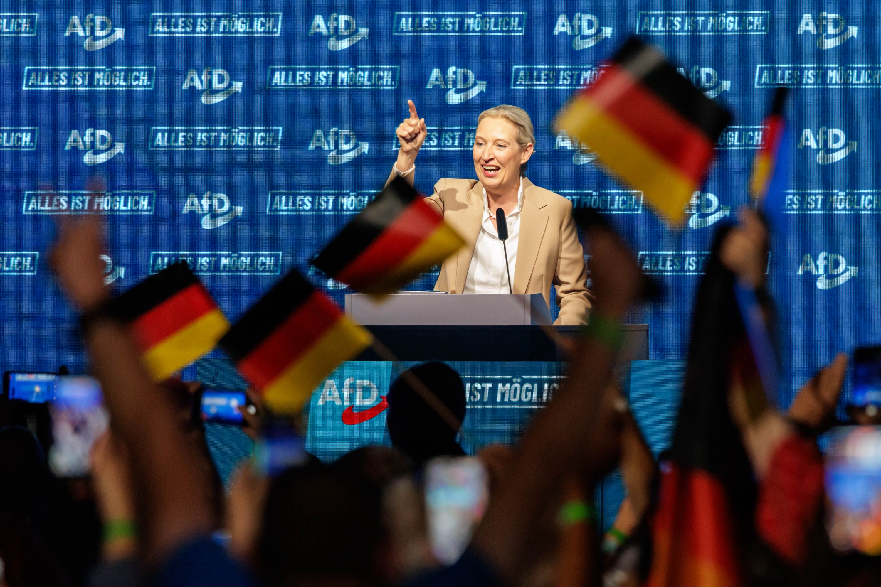 Eine Rednerin spricht auf einer AfD-Veranstaltung vor jubelndem Publikum mit Deutschlandflaggen.