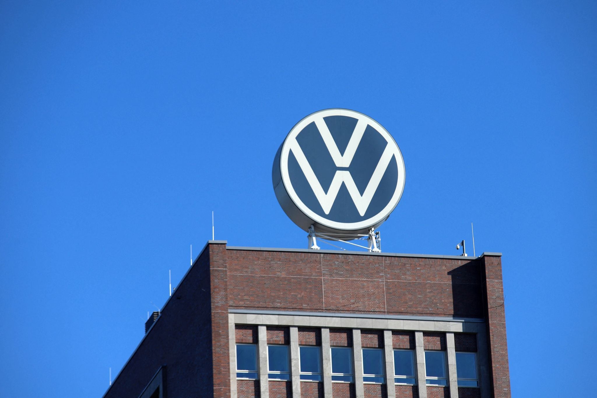 Das Volkswagen-Logo ist auf dem Dach eines Backsteingebäudes bei klarem, blauem Himmel zu sehen.