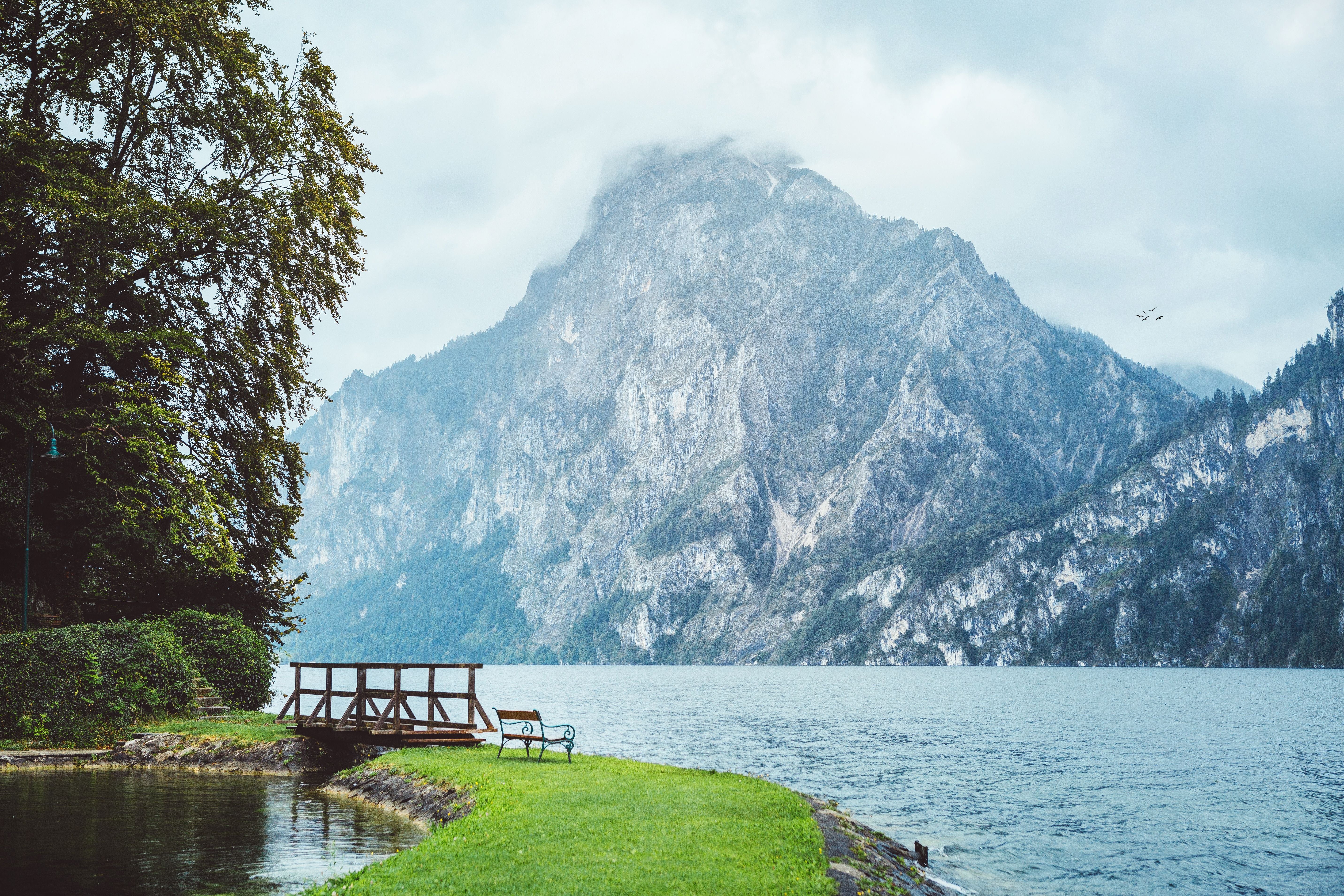 Holzbank und Brücke am Seeufer mit Blick auf nebelbedeckten Berg am Traunsee in Österreich.