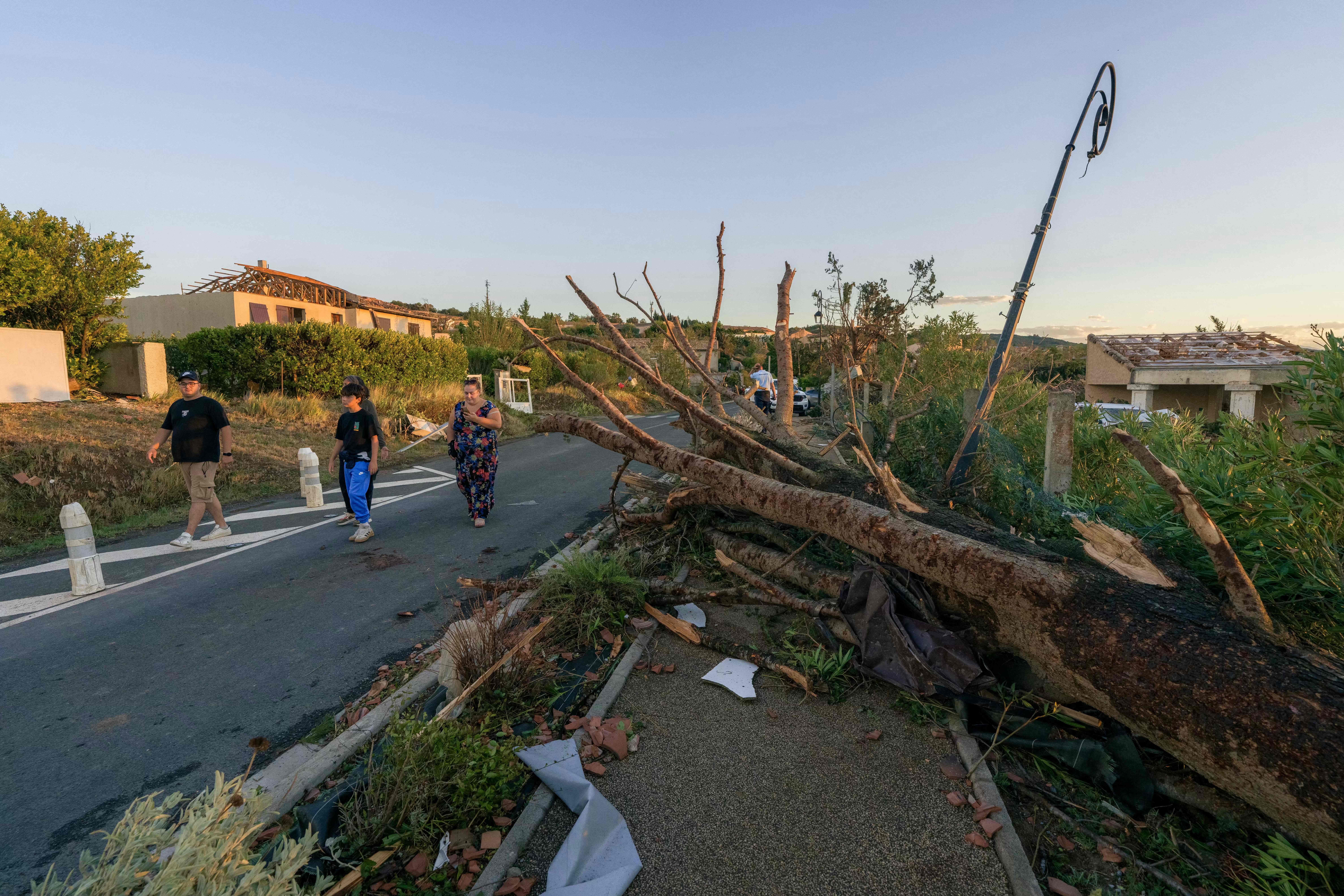 Menschen gehen an einem umgestürzten Baum und Sturmschäden in einem Dorf vorbei.