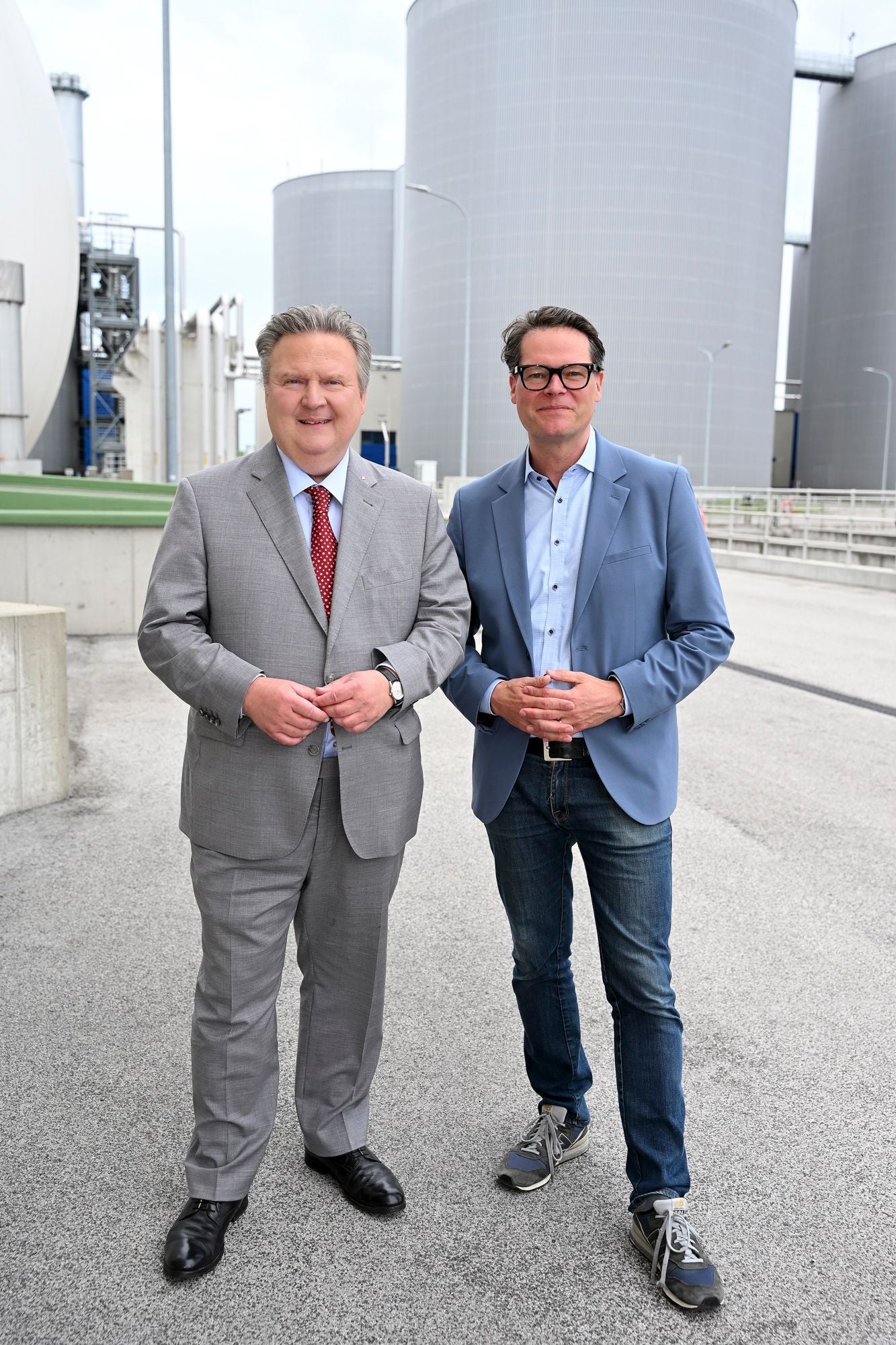 Zwei Männer stehen vor großen Silos auf dem Gelände einer Solaranlage.