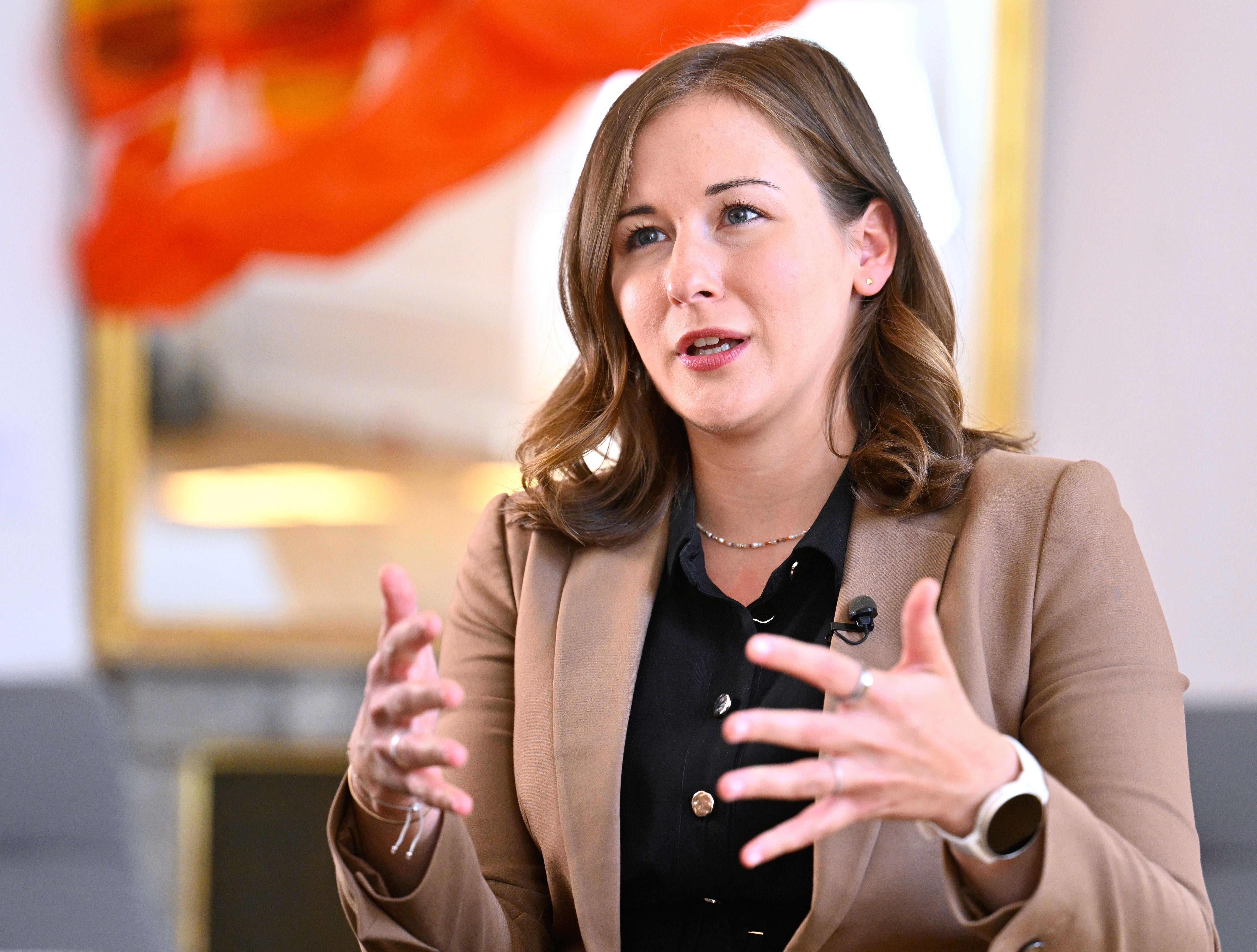 Eine Frau im beigen Blazer spricht gestikulierend während eines Interviews.