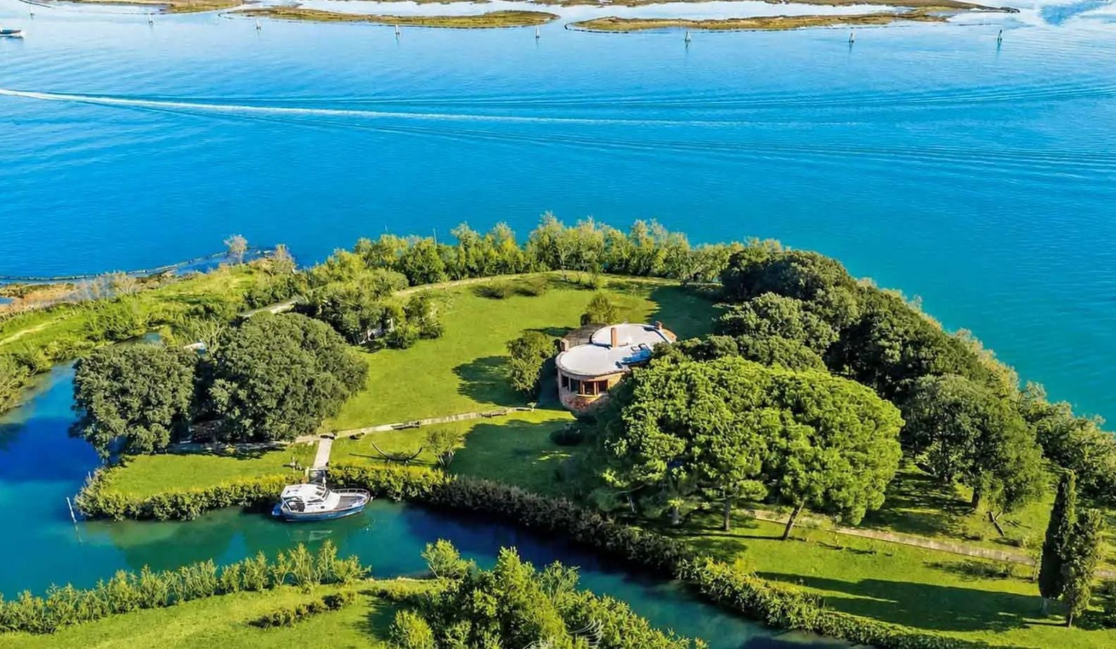 Luftaufnahme der Isola di Crevan mit Haus, Bootsanleger und üppigem Grün am Wasser.