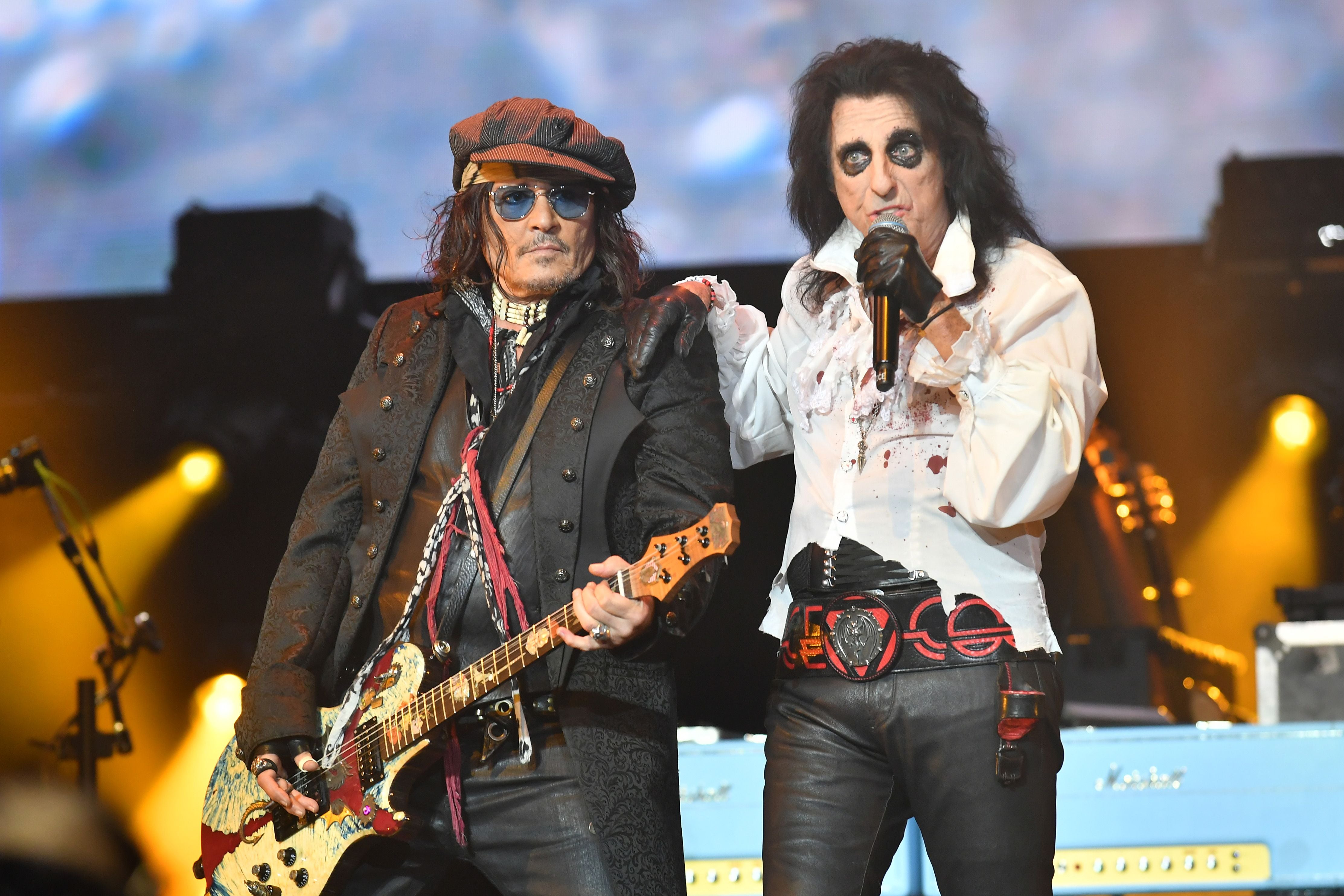 Zwei Musiker der Band Hollywood Vampires treten auf einer Bühne mit Gitarre und Mikrofon auf.