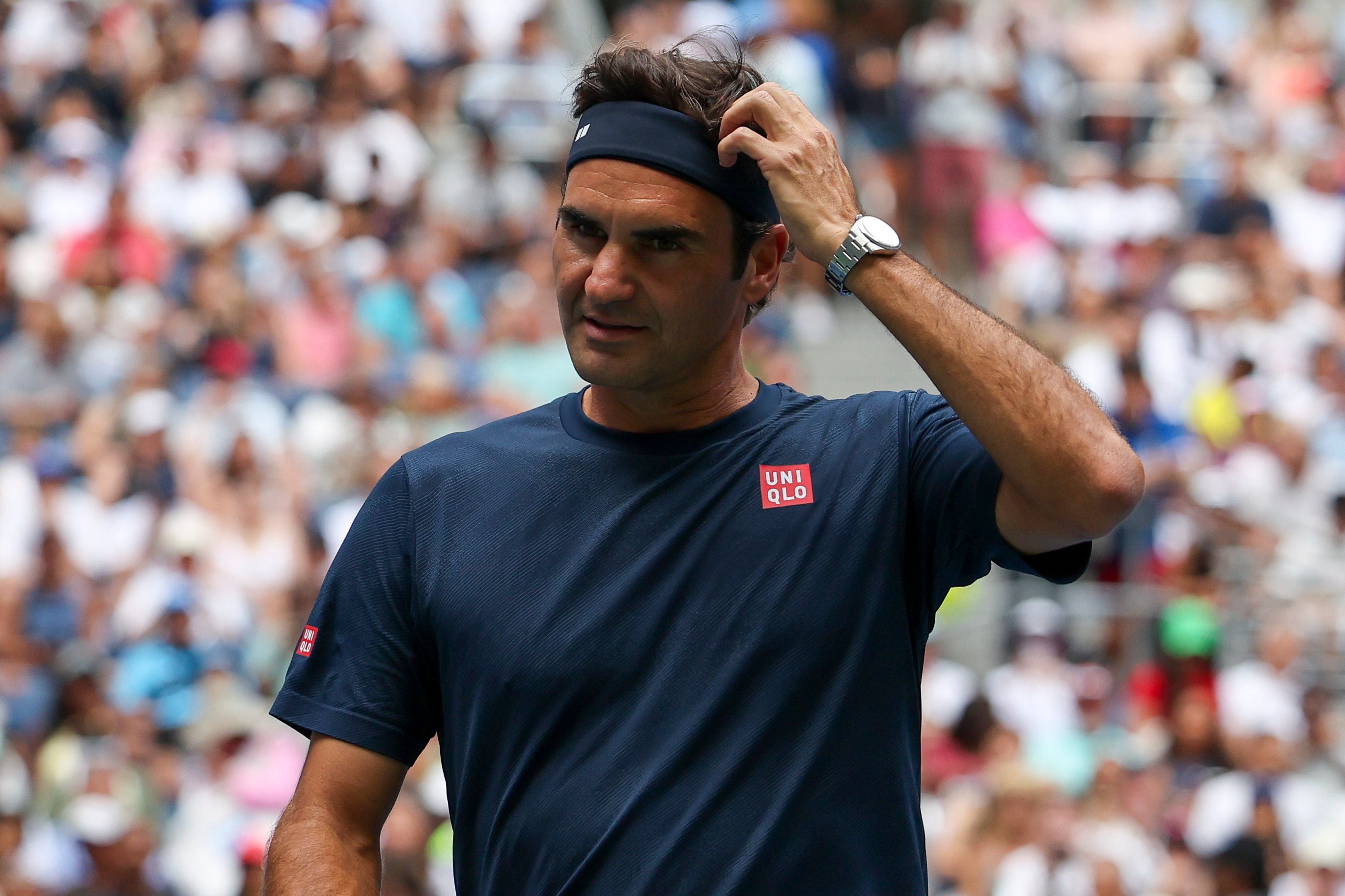 Ein Tennisspieler im blauen Shirt kratzt sich am Kopf auf einem Tennisplatz mit Publikum.
