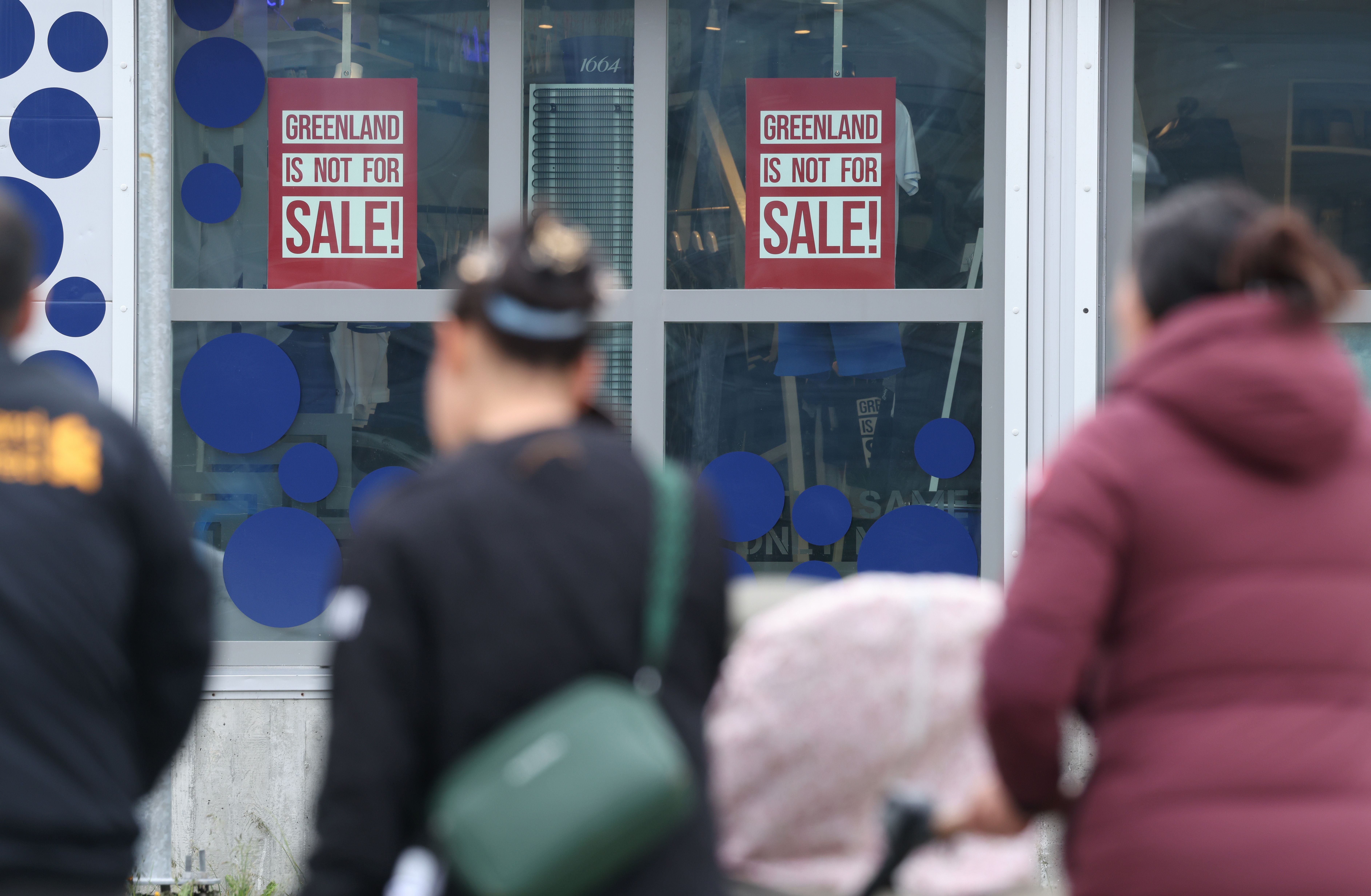 Eine Familie läuft an Schildern vorbei, auf denen "Greenland is not for sale!" steht.