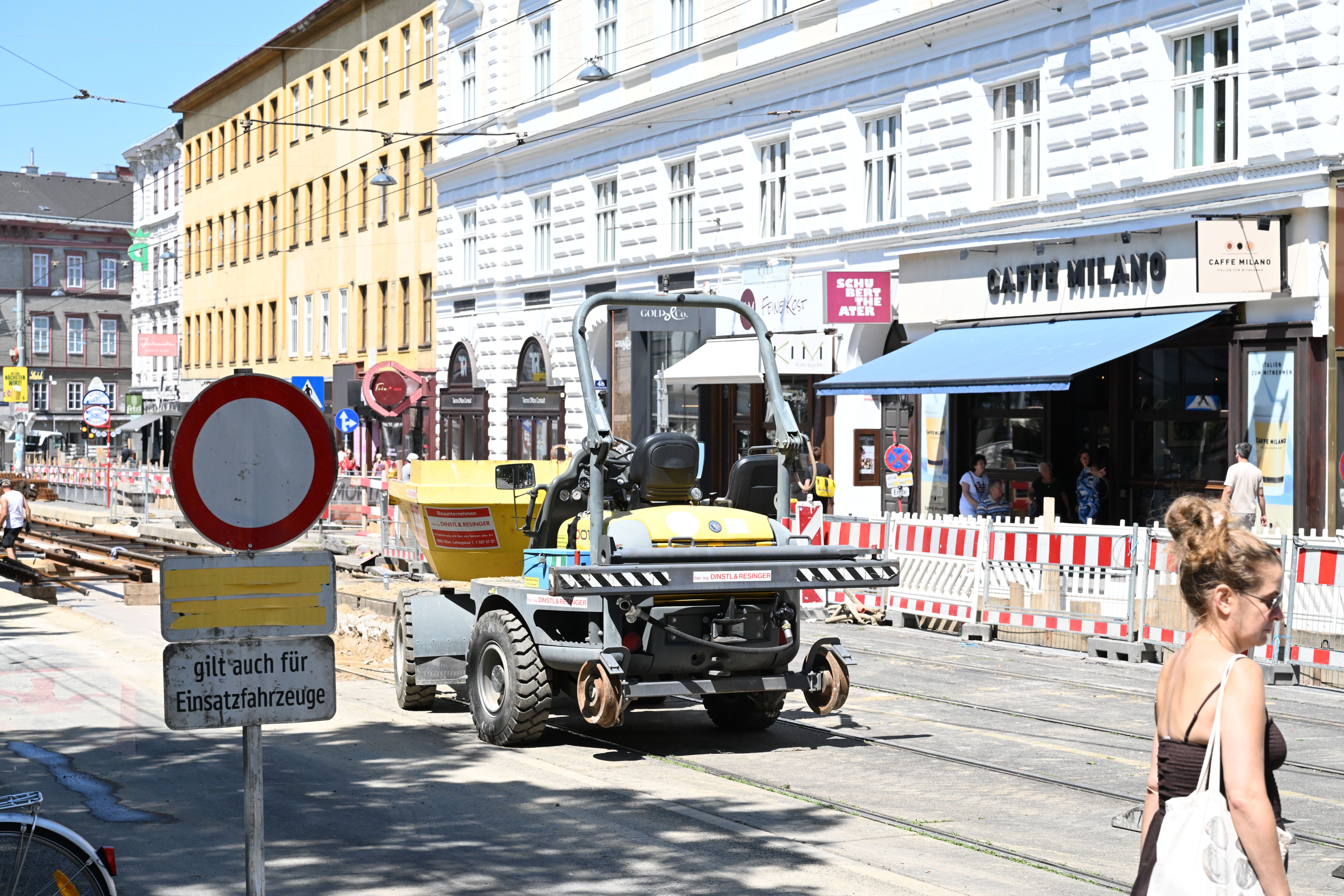 Baustelle auf der Währingerstraße mit Baufahrzeug, Absperrungen und Fußgängerin im Vordergrund.