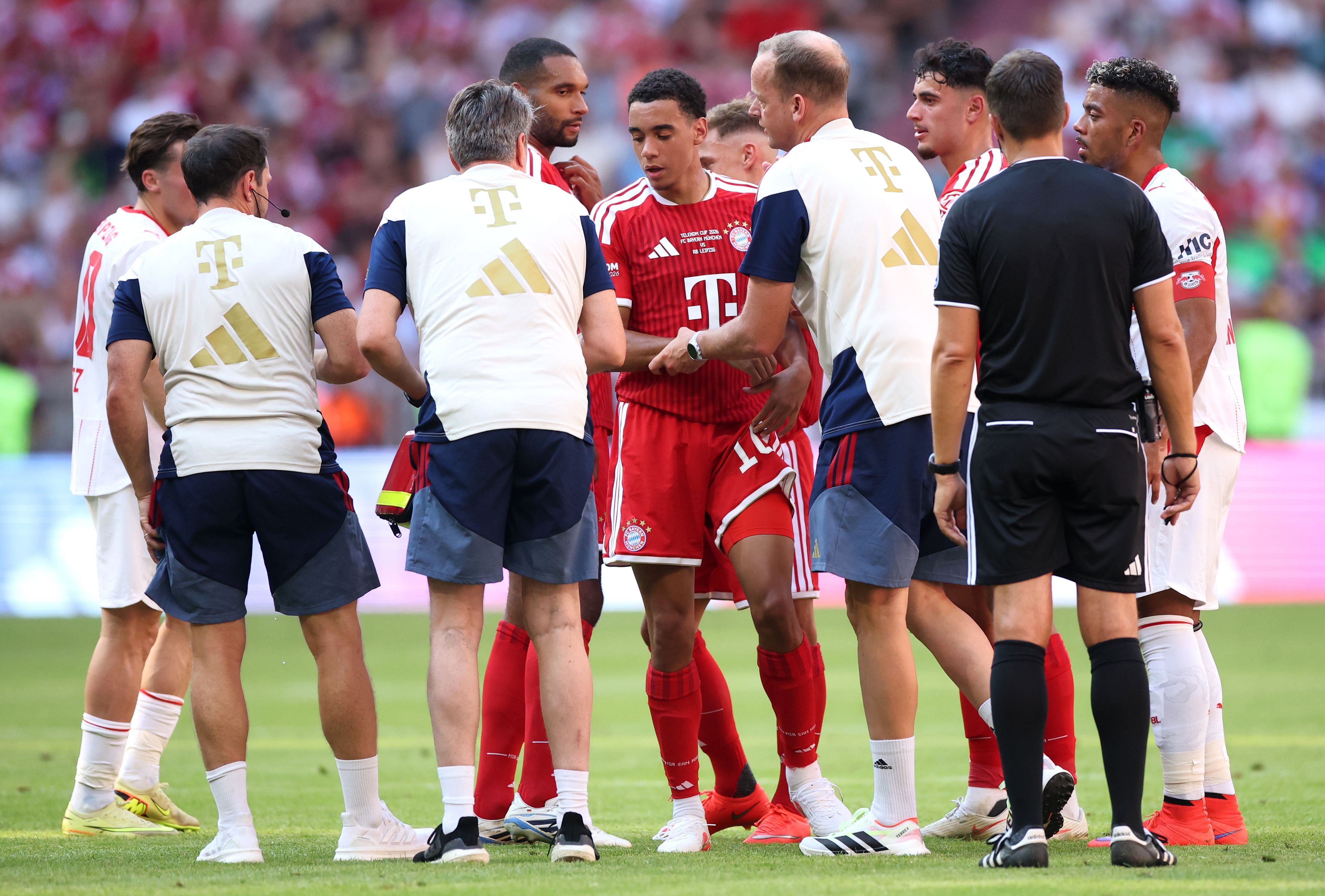 Jamal Musiala von Bayern München wird nach einer Verletzung von Betreuern auf dem Spielfeld unterstützt.