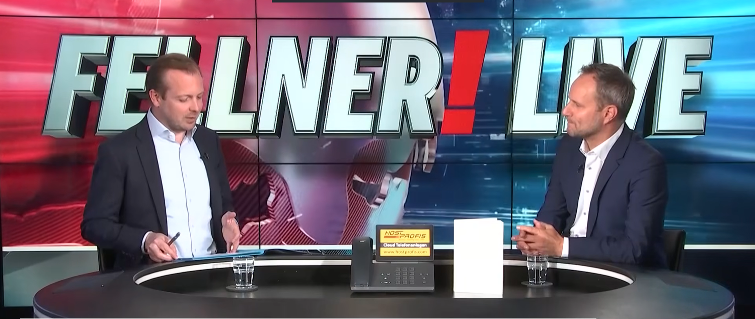 Zwei Männer im Anzug sitzen in einem Fernsehstudio mit dem Schriftzug „Fellner! Live“.