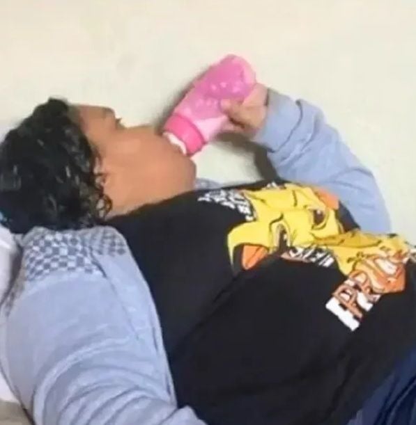 Eine Person liegt und trinkt aus einer rosa Babyflasche.