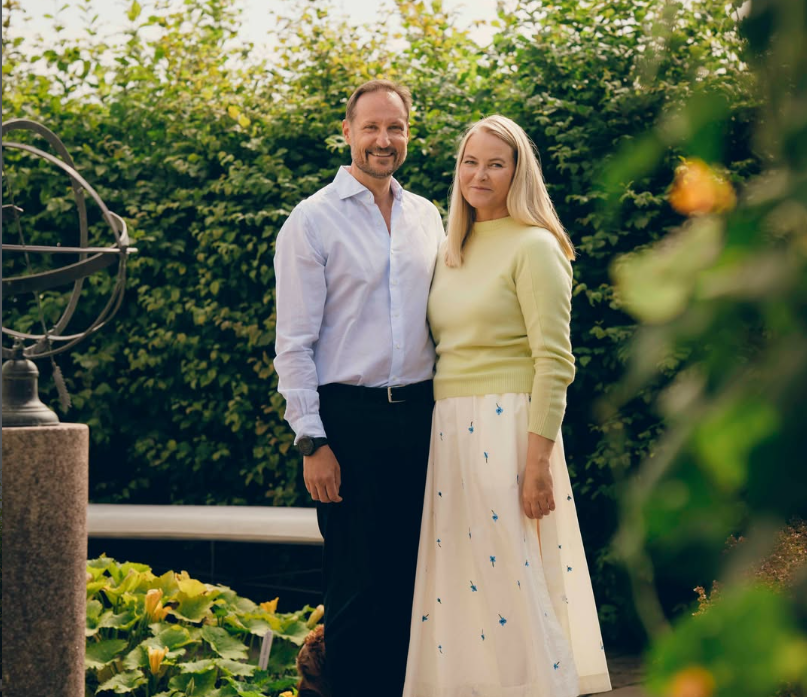 Ein Mann und eine Frau stehen nebeneinander in einem Garten vor einer grünen Hecke.