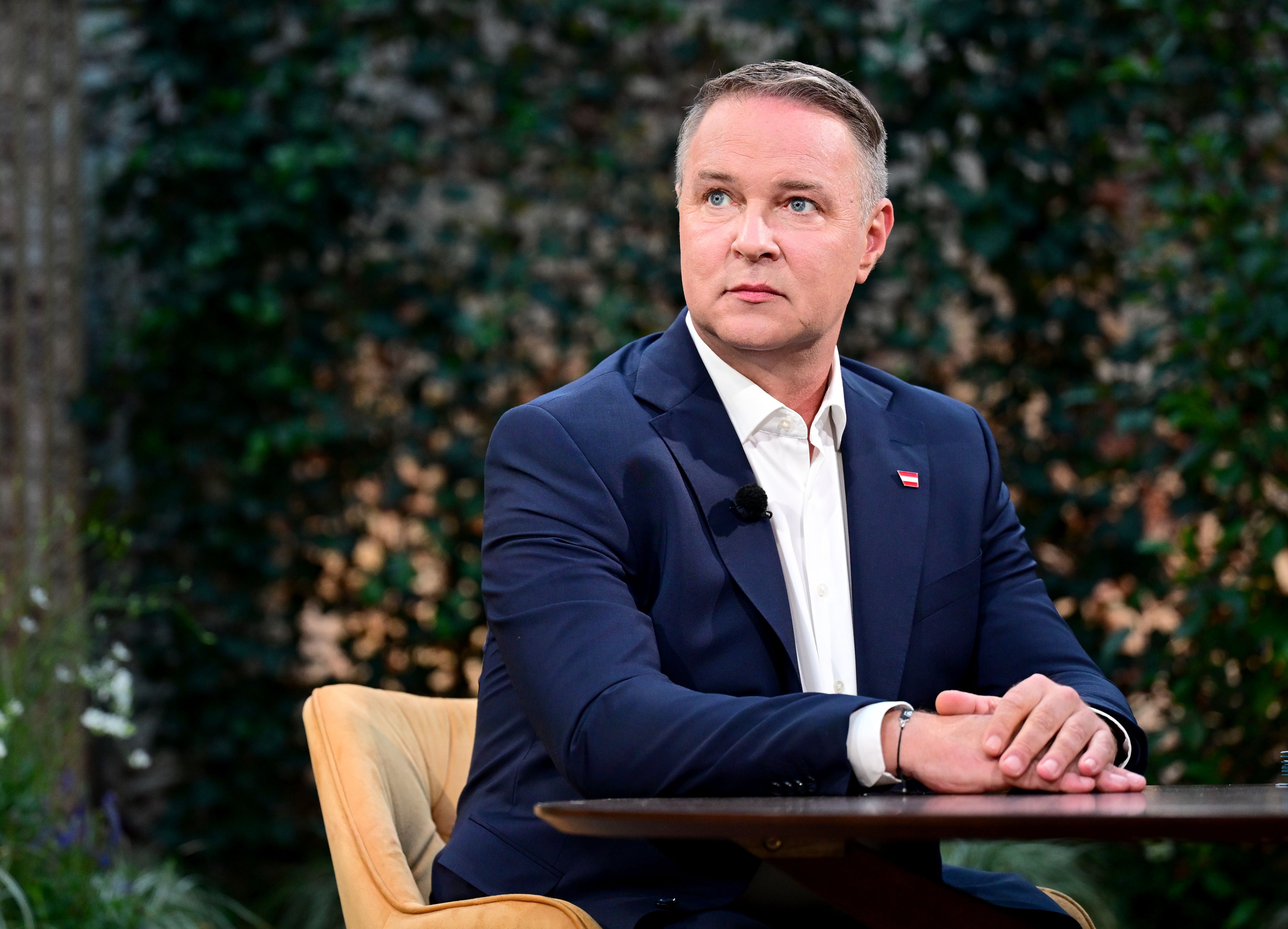 Ein Mann im blauen Anzug sitzt an einem Tisch und schaut ernsthaft zur Seite.