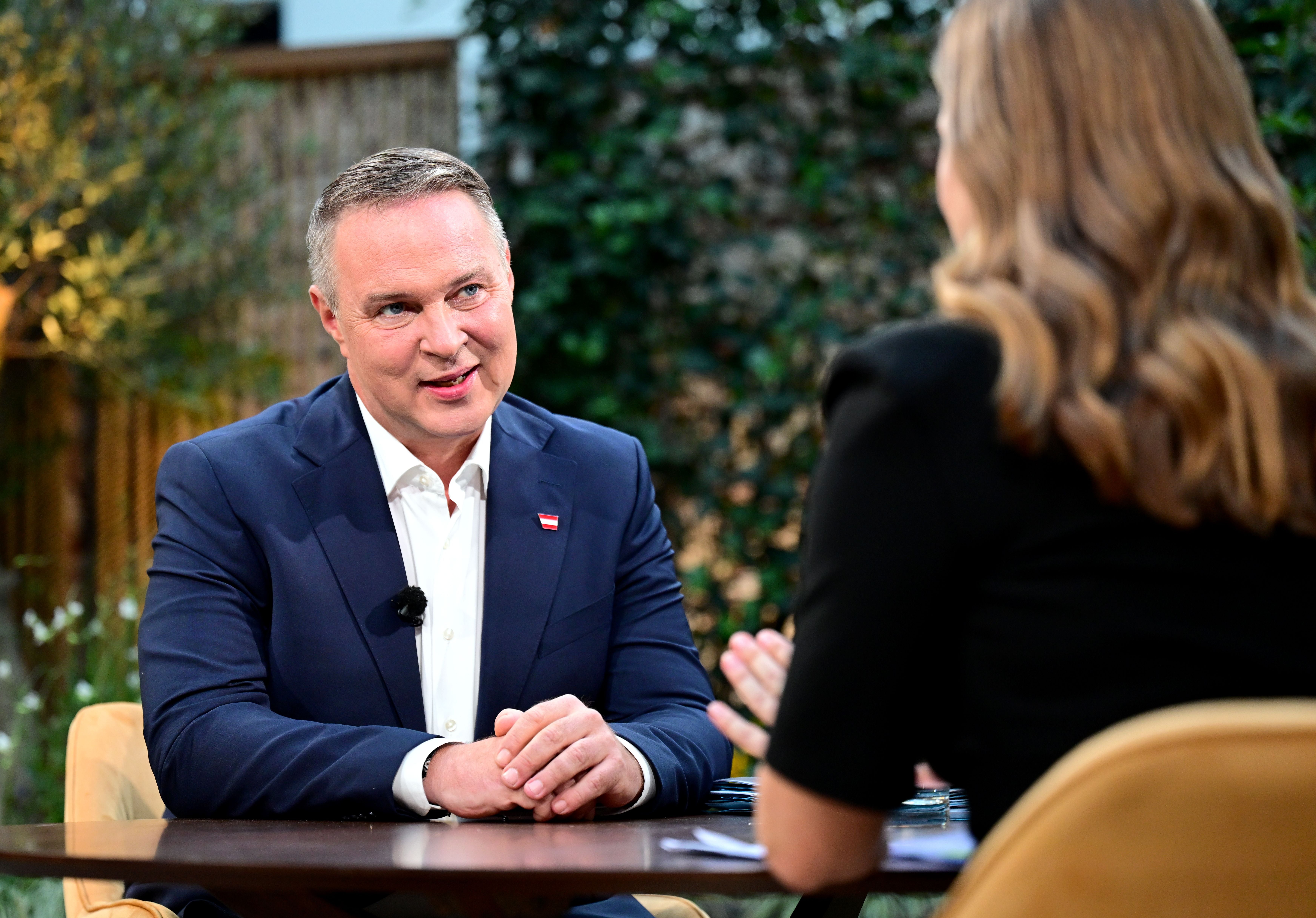 Ein Mann im Anzug spricht in einem Interview mit einer Frau in einem Gartenambiente.