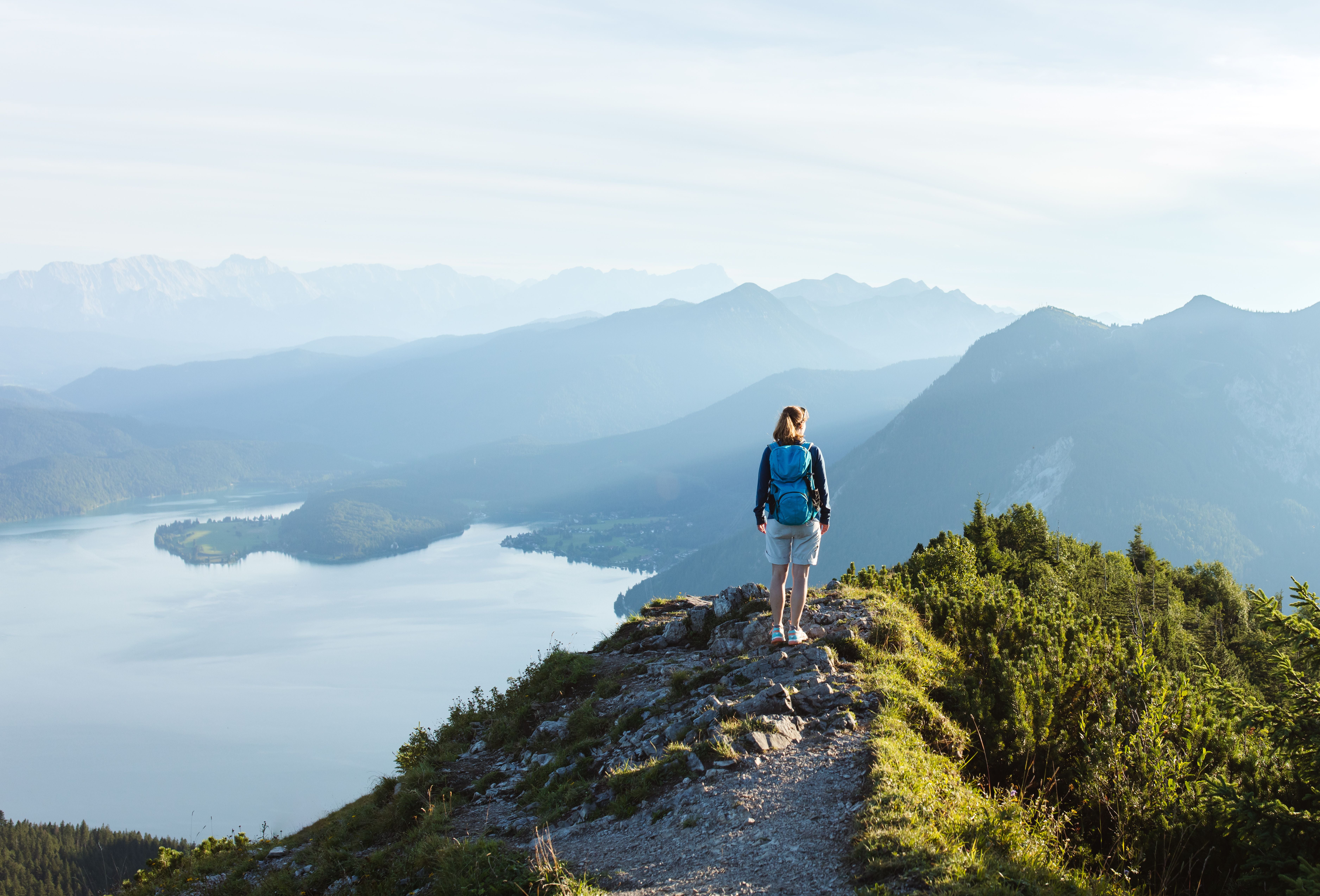 Frau mit Rucksack wandert auf einem Berg mit Blick auf See und umliegende Berge.