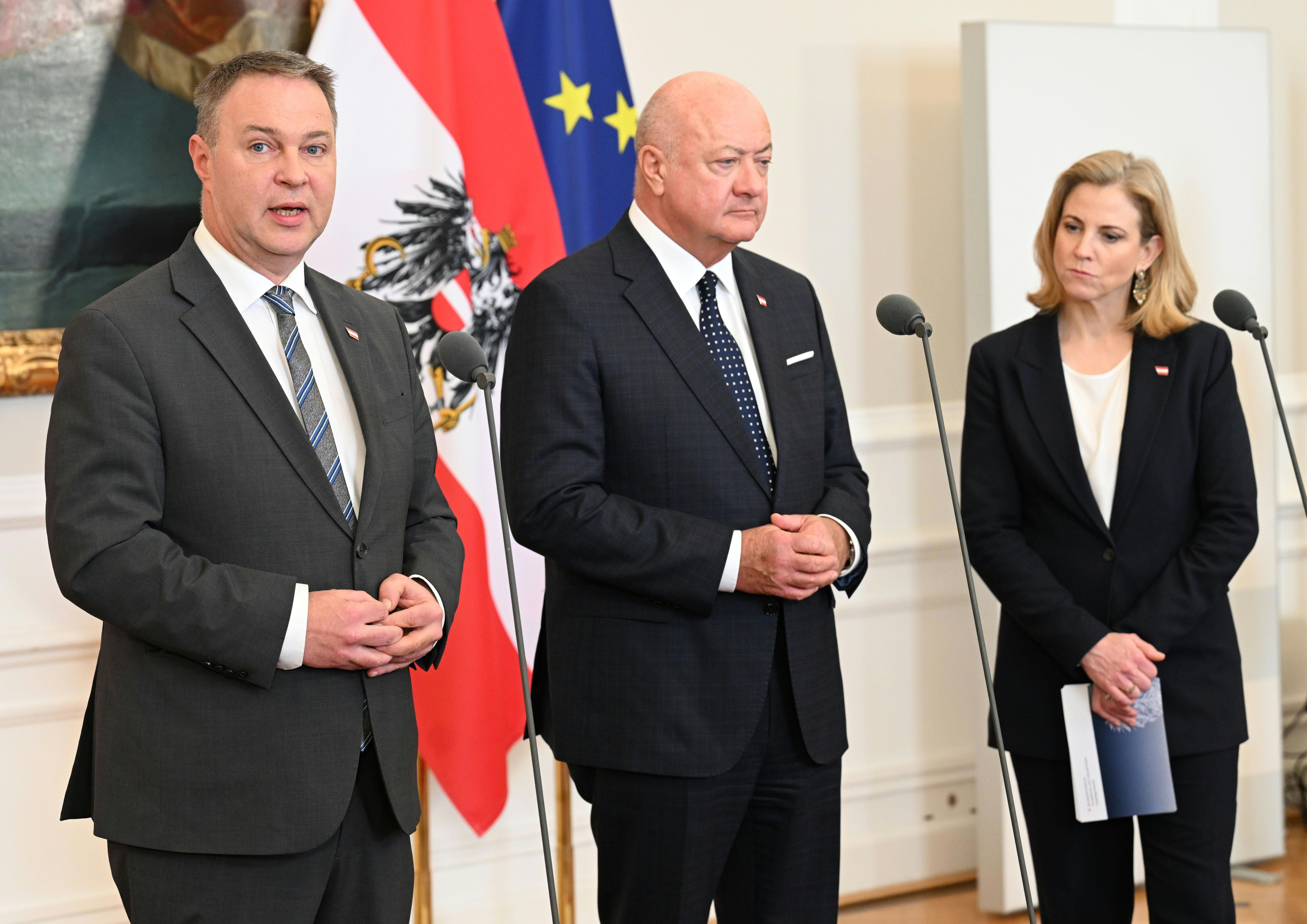 Drei Politiker stehen im Anzug vor Mikrofonen im Bundeskanzleramt in Wien.