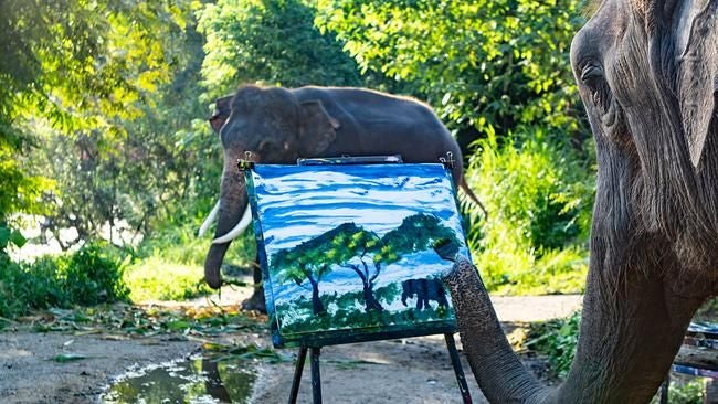 Ein Elefant malt mit dem Rüssel ein Landschaftsbild auf einer Staffelei, im Hintergrund steht ein weiterer Elefant.