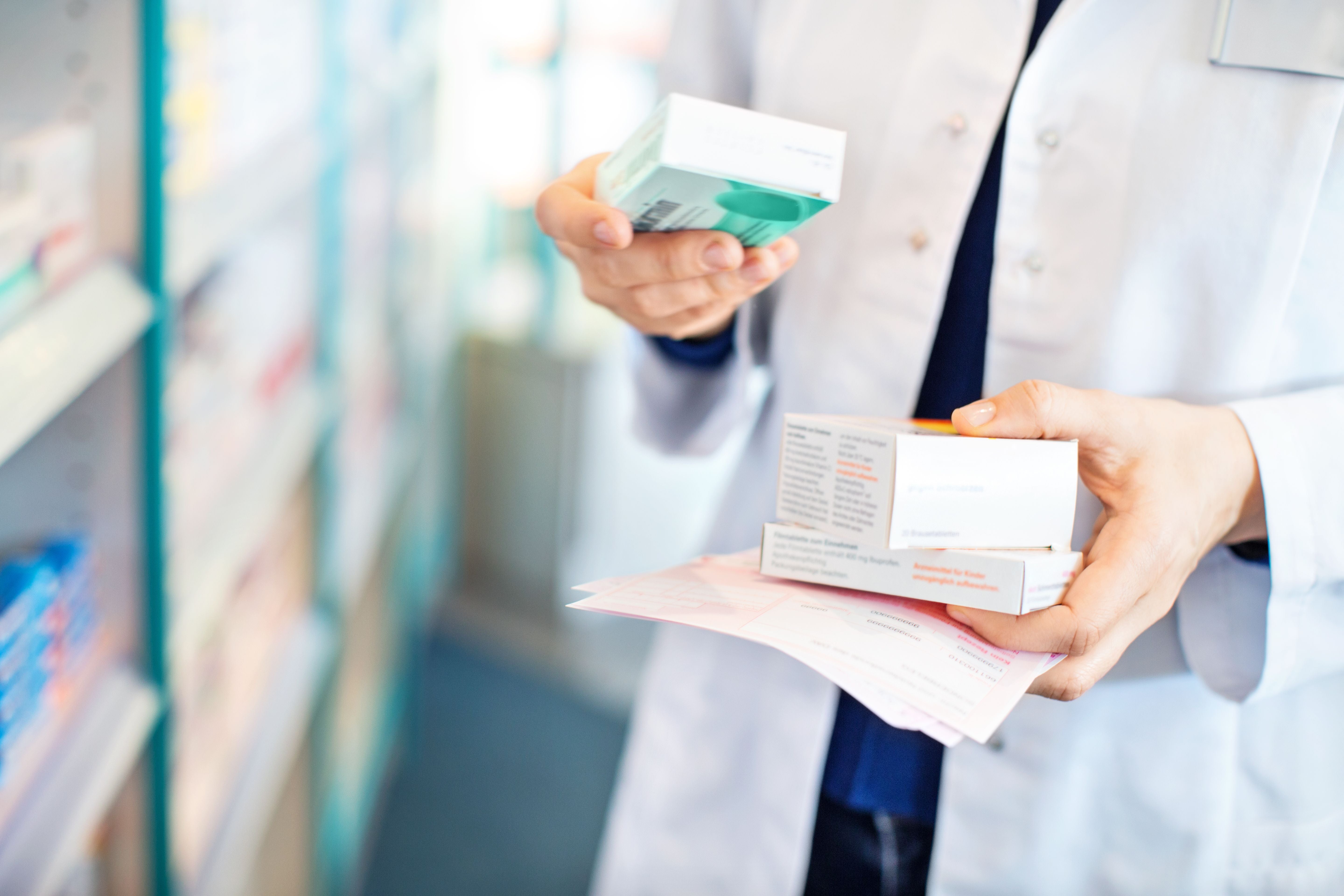 Nahaufnahme von Händen eines Apothekers, der Medikamente im Regal einer Apotheke hält.