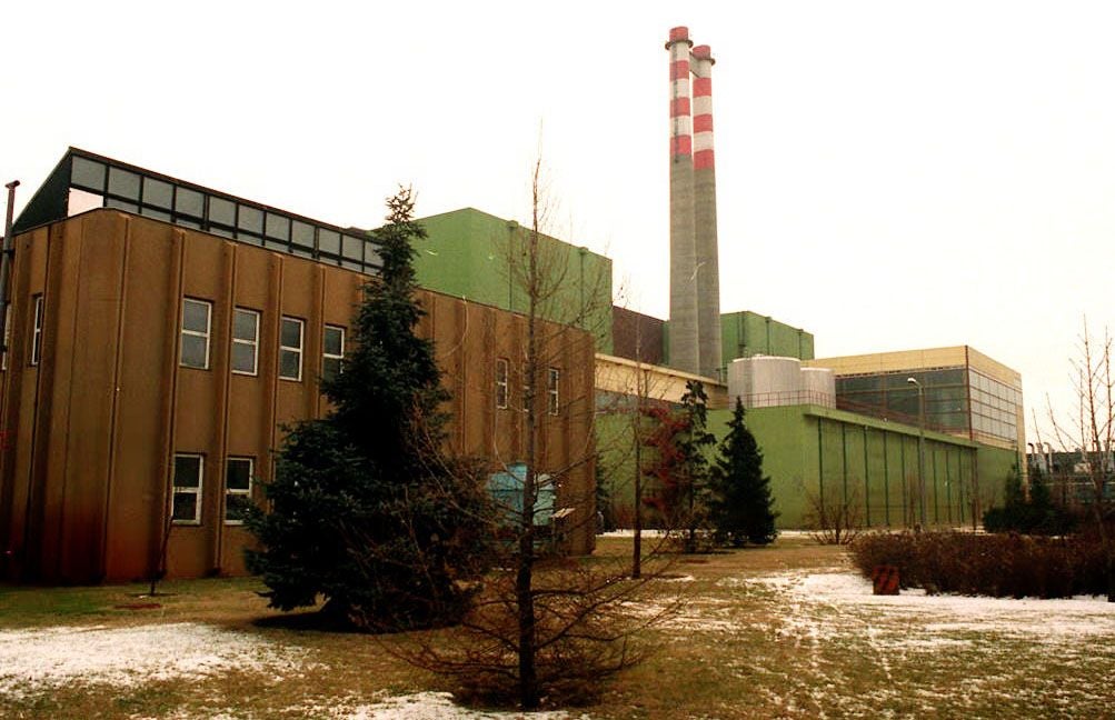Atomkraftwerk mit Schornstein und grünen Gebäuden, umgeben von Bäumen im Winter.