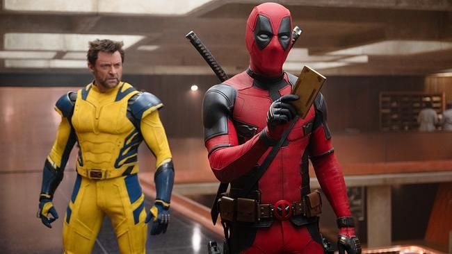 Deadpool schaut auf ein Handy, während Wolverine in gelbem Anzug daneben steht.