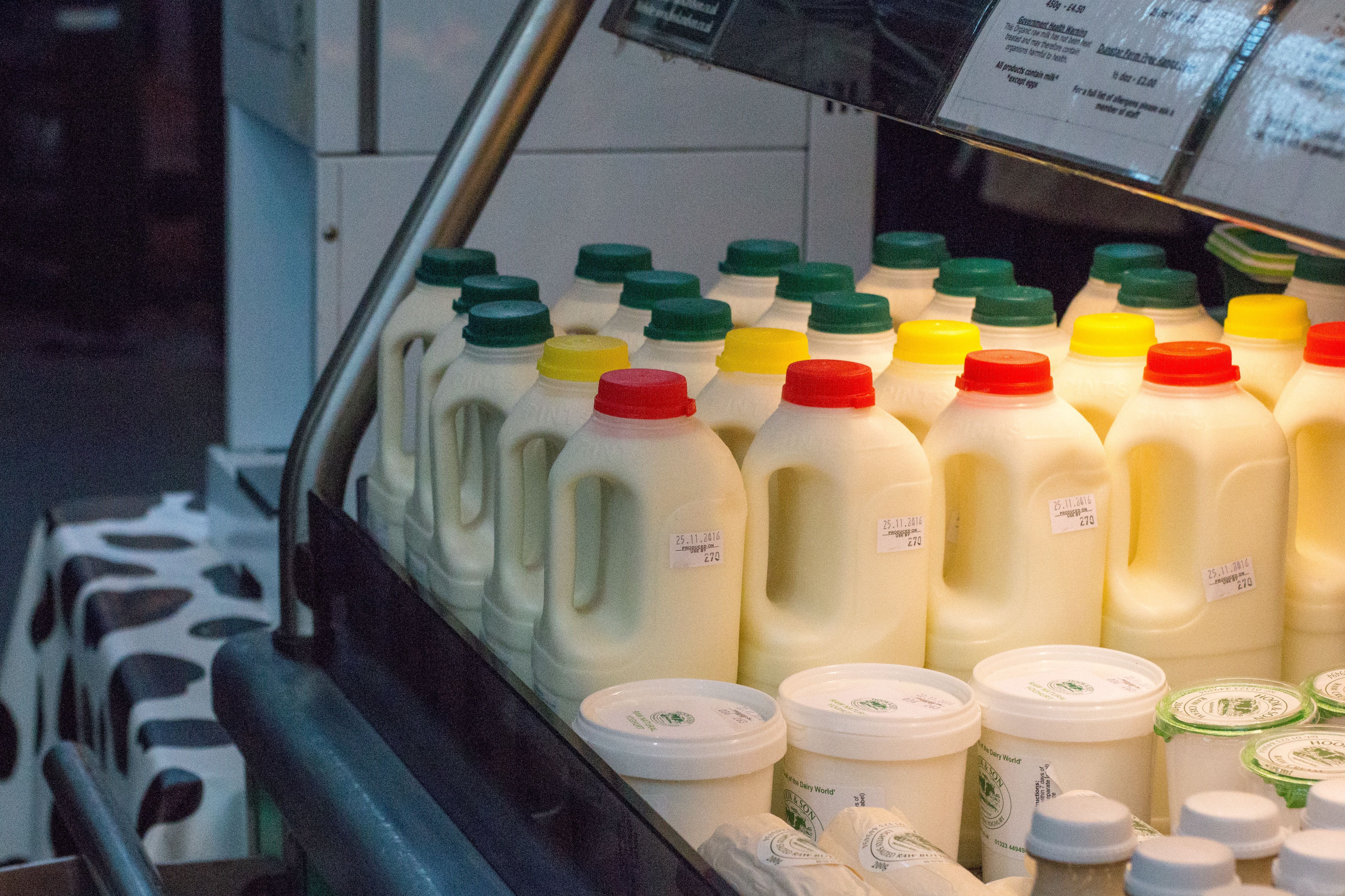Milchflaschen mit bunten Deckeln stehen in einem Markt-Kühlregal neben Joghurtbechern.