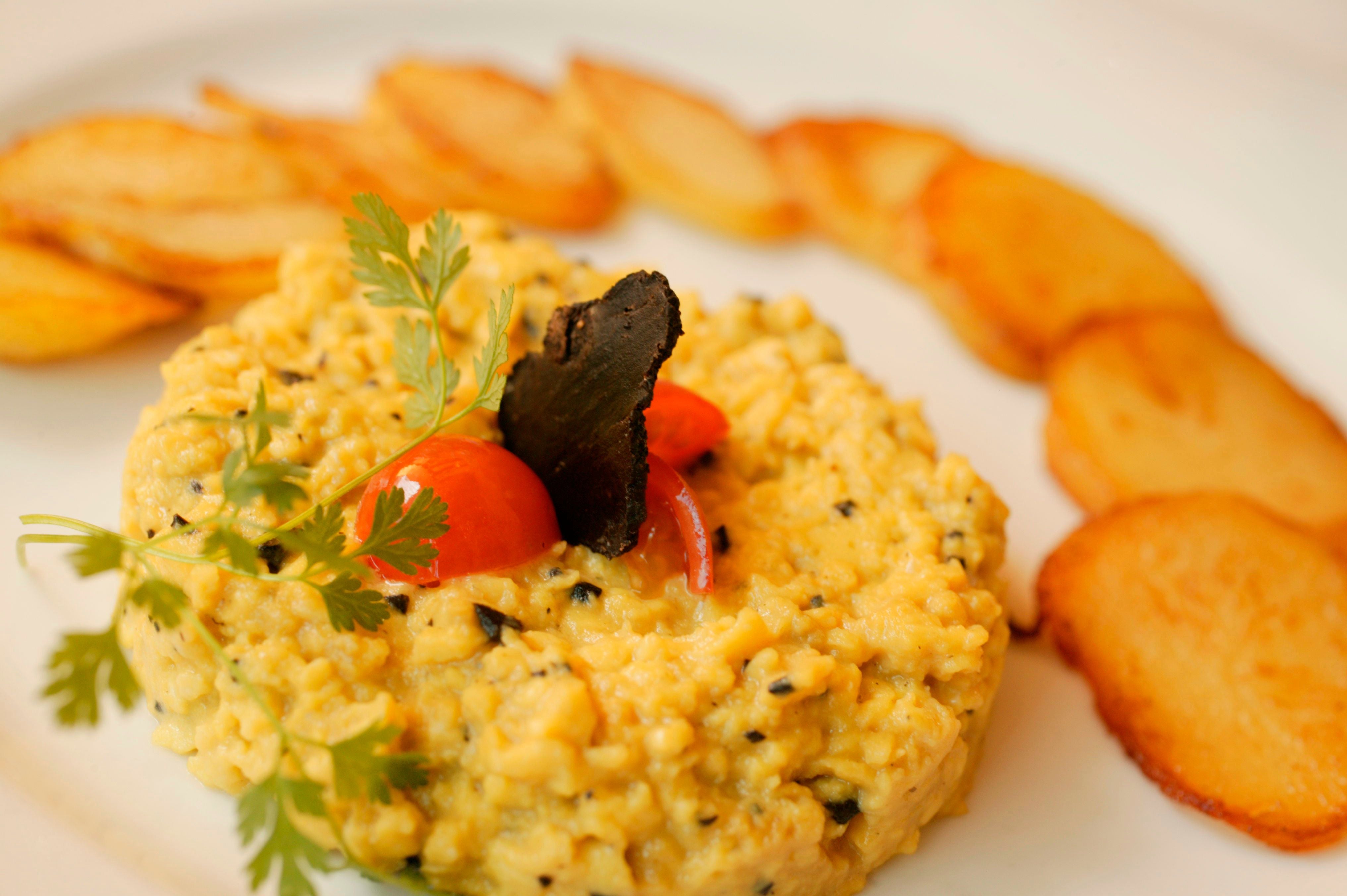 Brouillade mit schwarzen Trüffeln und Kartoffelscheiben, garniert mit Kräutern und Tomate.